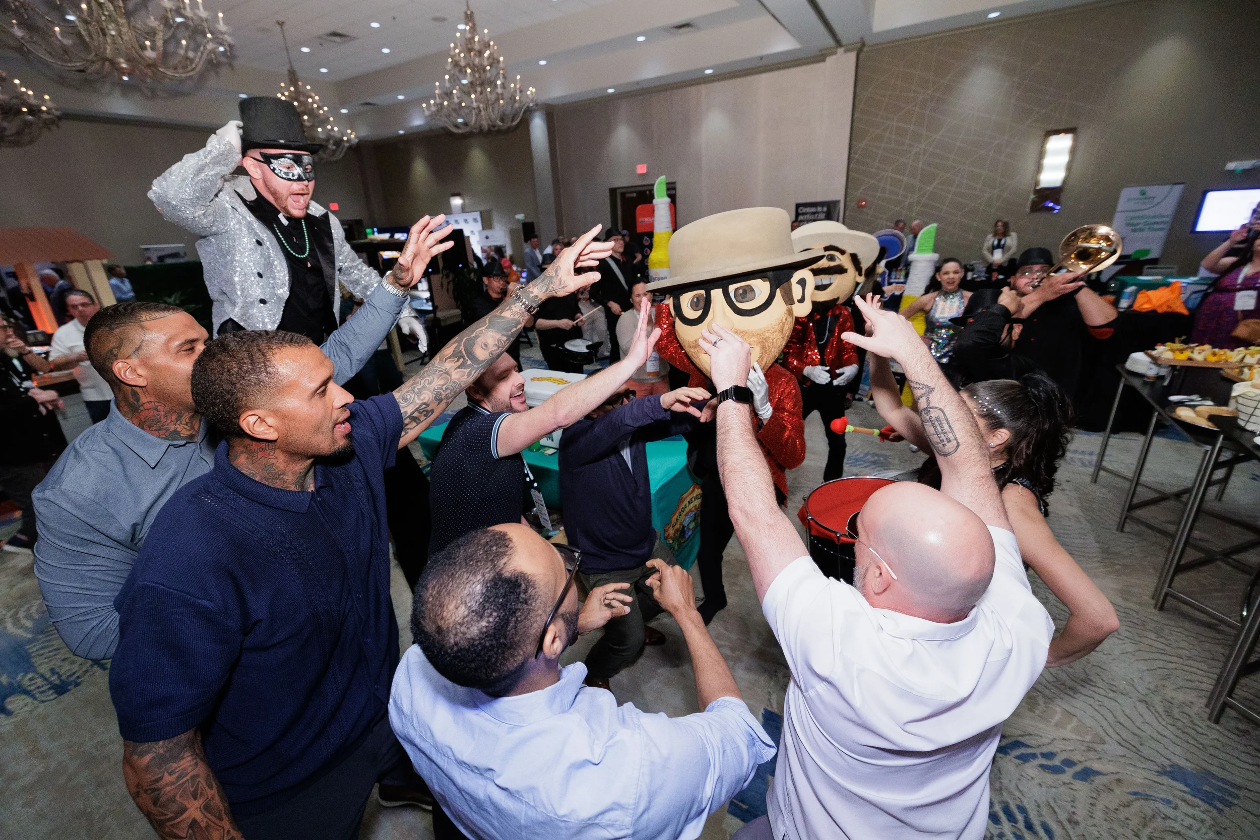 Group of attendees celebrate with mascots and stilt performer on expo floor at Orlando industry conference