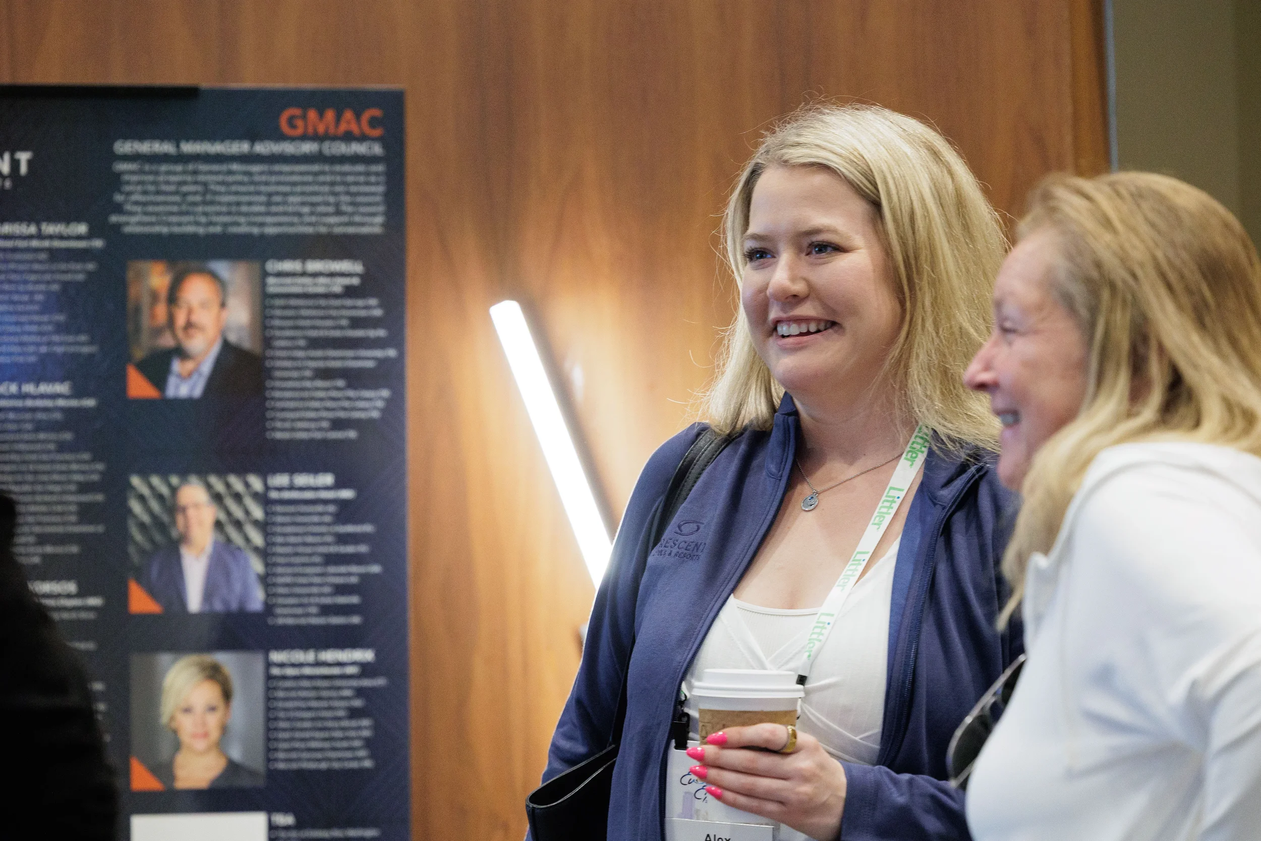 Two female attendees with lanyards laugh together near branded advisory council signage at Orlando corporate conference