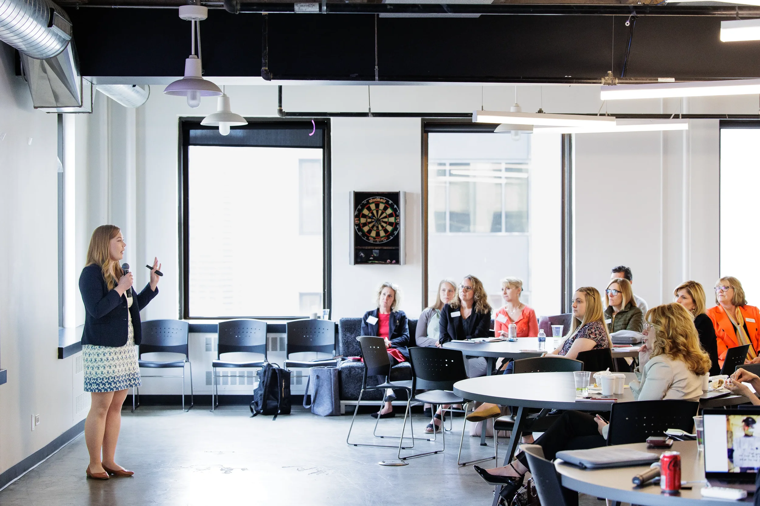 Female speaker gestures with microphone while addressing a full seated audience at Chicago conference