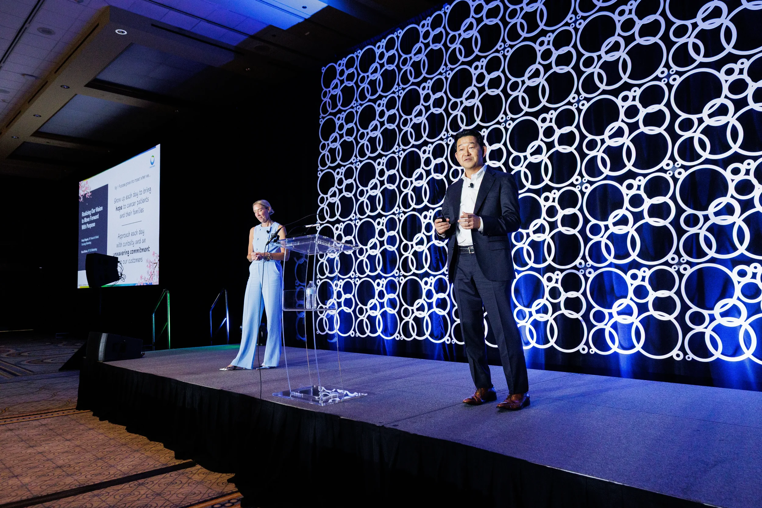 Speakers present on stage with circular backdrop during Orlando corporate conference