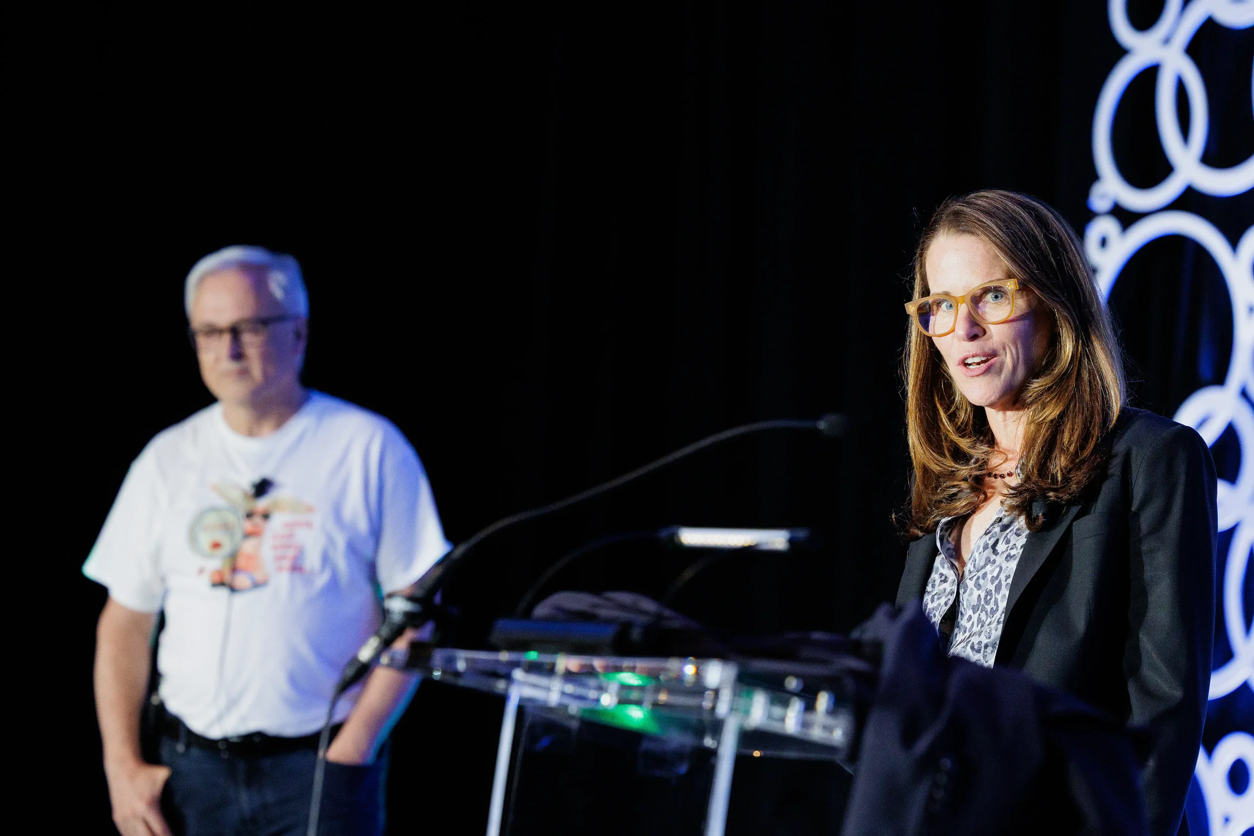 Speaker presents from podium with branded circle backdrop at Orlando corporate conference