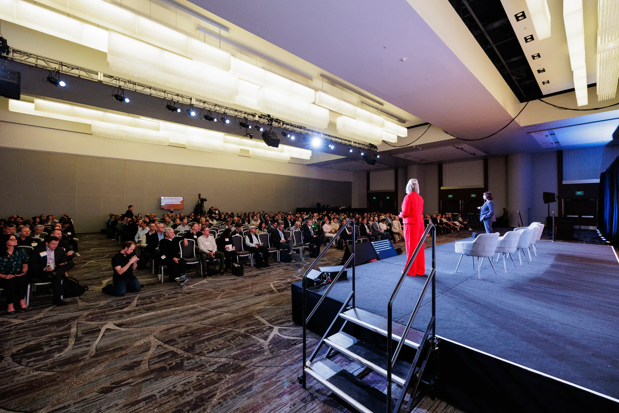 Speaker in red dress addresses packed ballroom audience from stage at Orlando corporate event