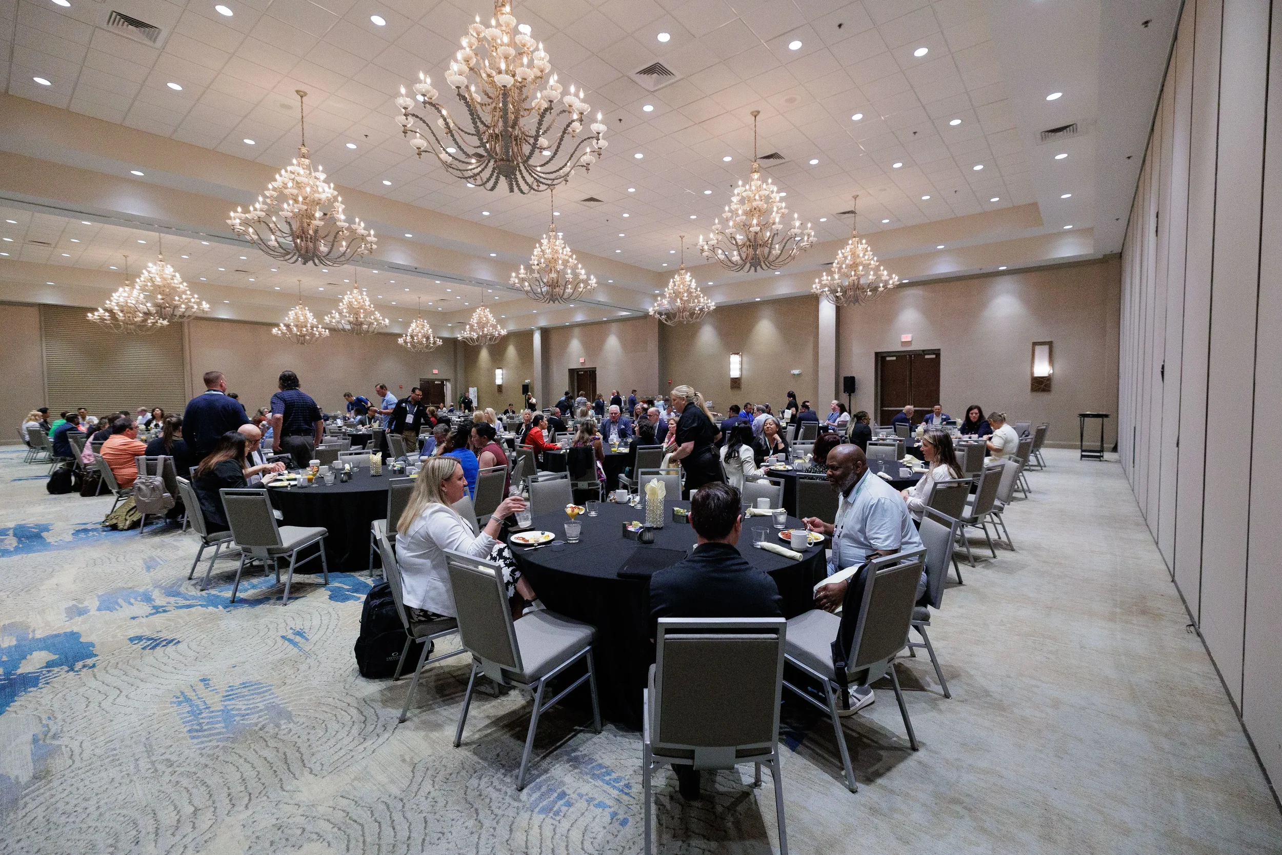 Attendees dine at round tables in large chandelier ballroom at Chicago corporate conference