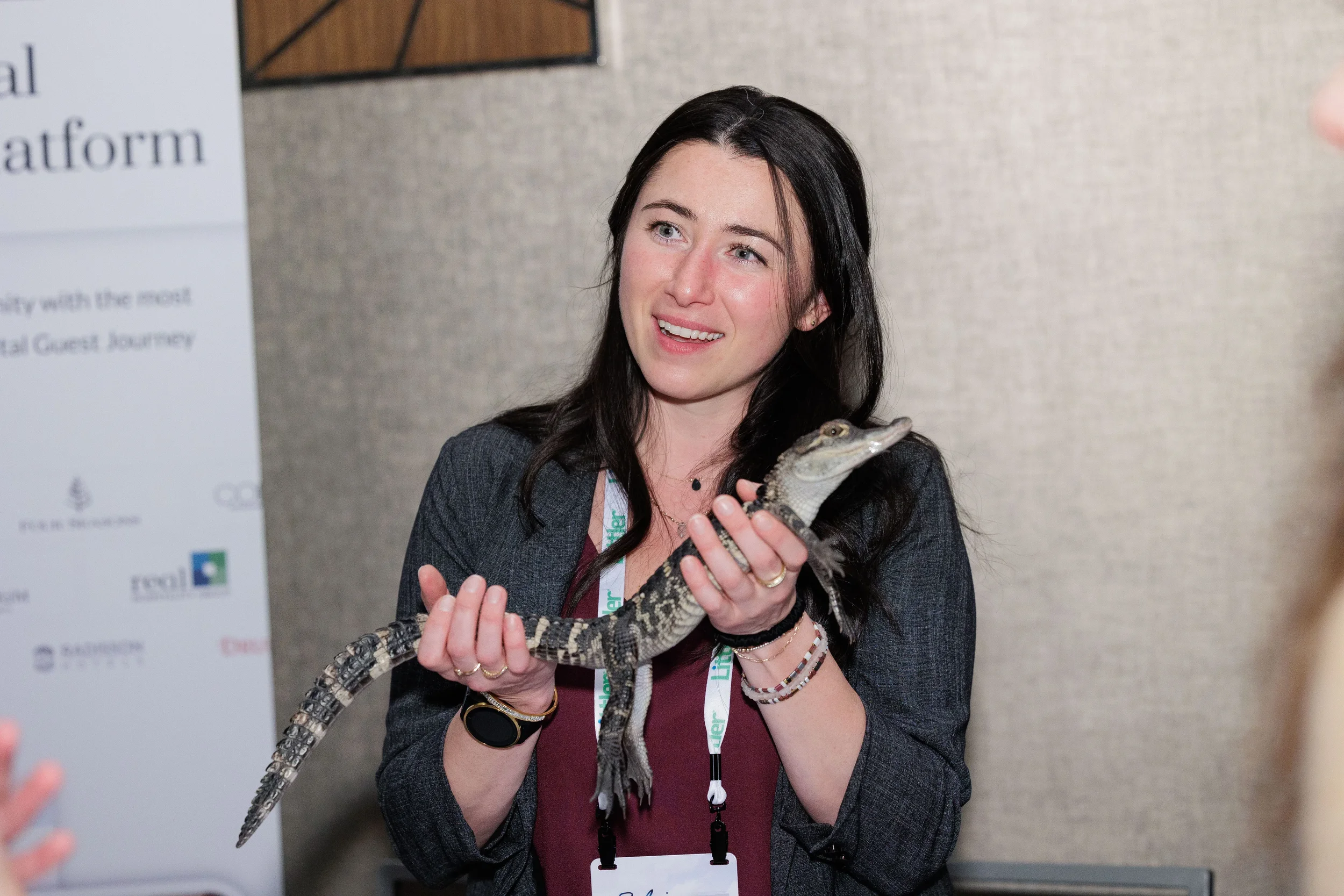 Female attendee with lanyard smiles while holding baby alligator at Orlando industry conference