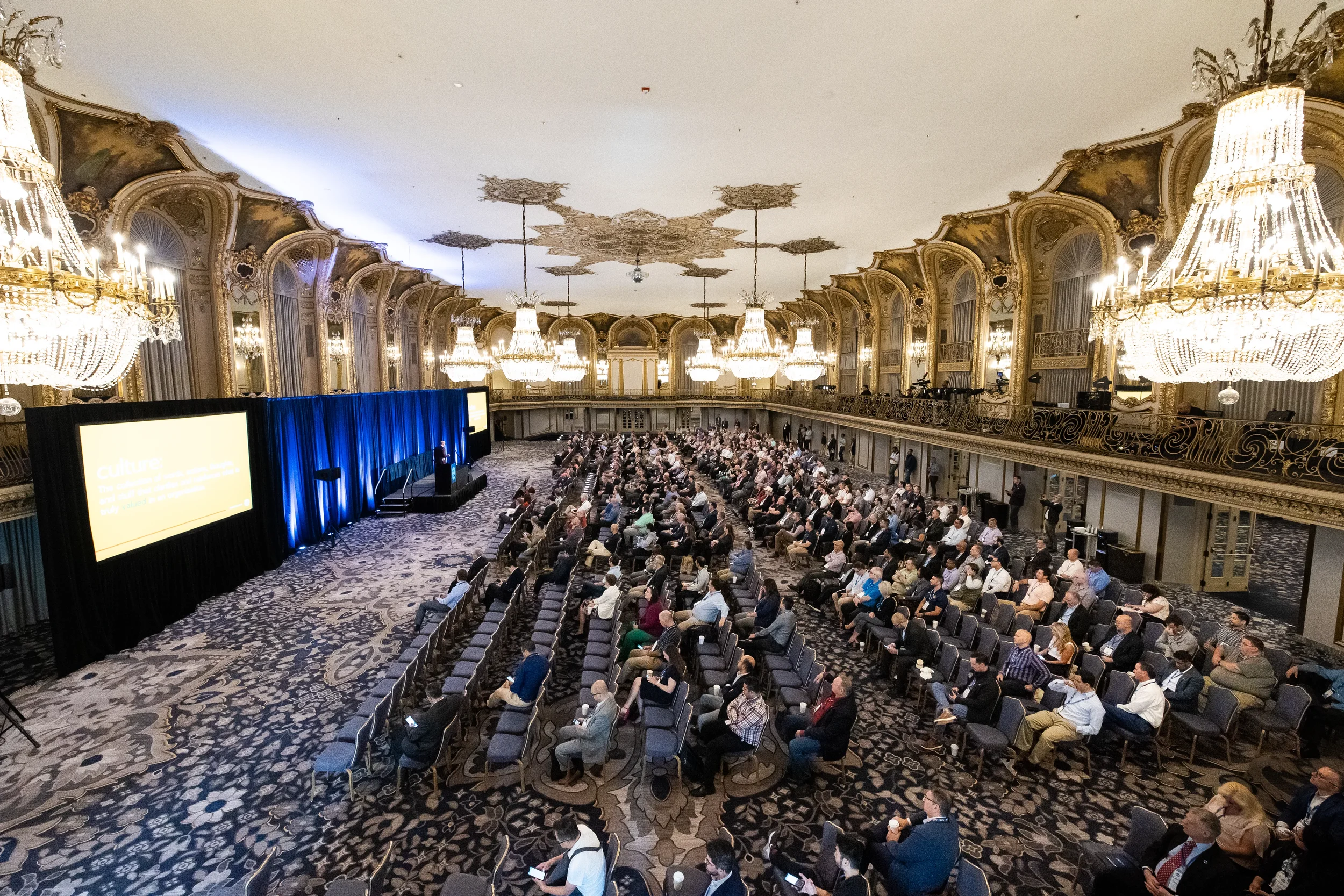 Speaker addresses seated audience from podium in ornate ballroom at Chicago corporate conference