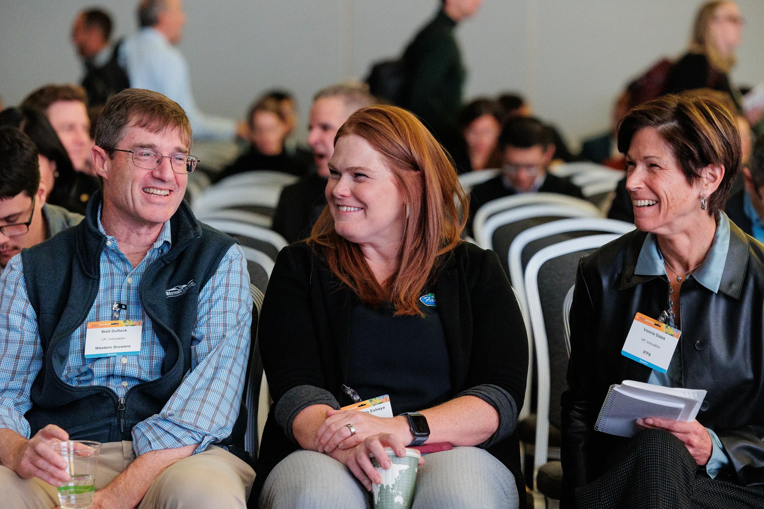 Three smiling badged attendees seated together laughing during Chicago corporate conference session