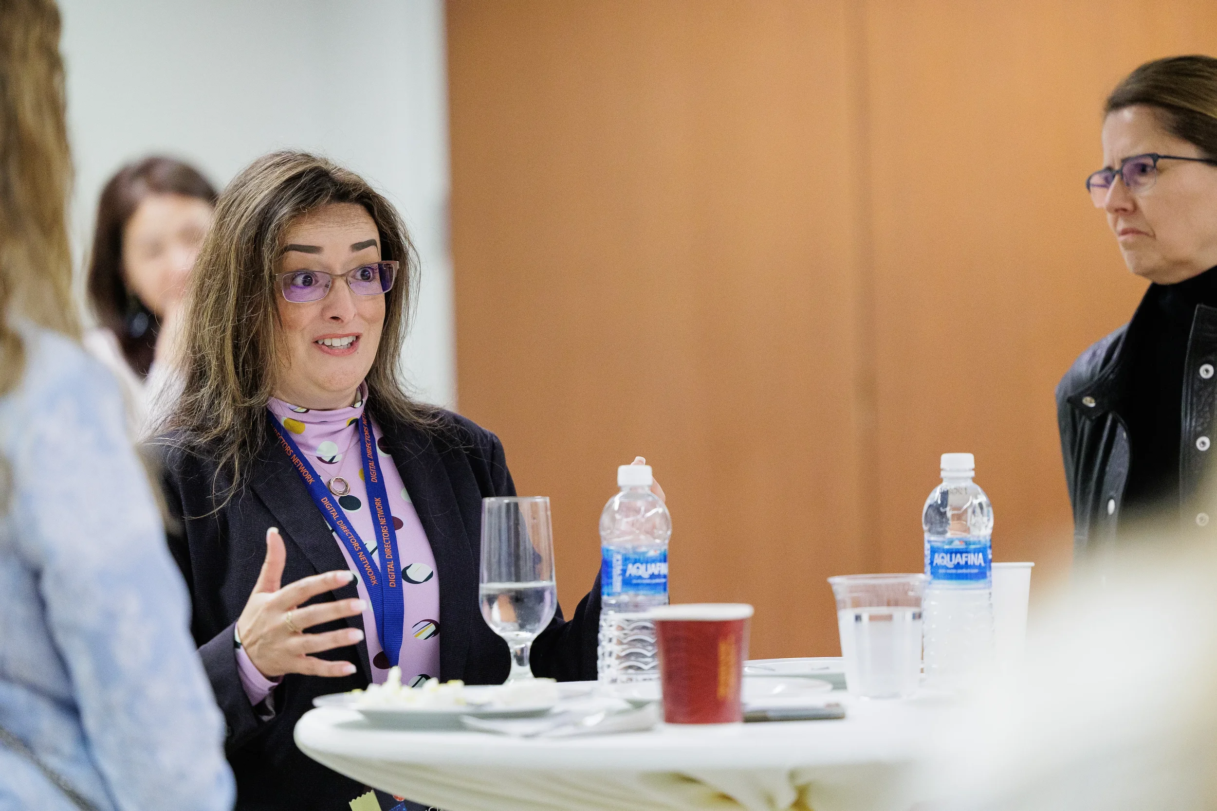 Female attendee with lanyard speaks animatedly at round table during Orlando corporate conference networking