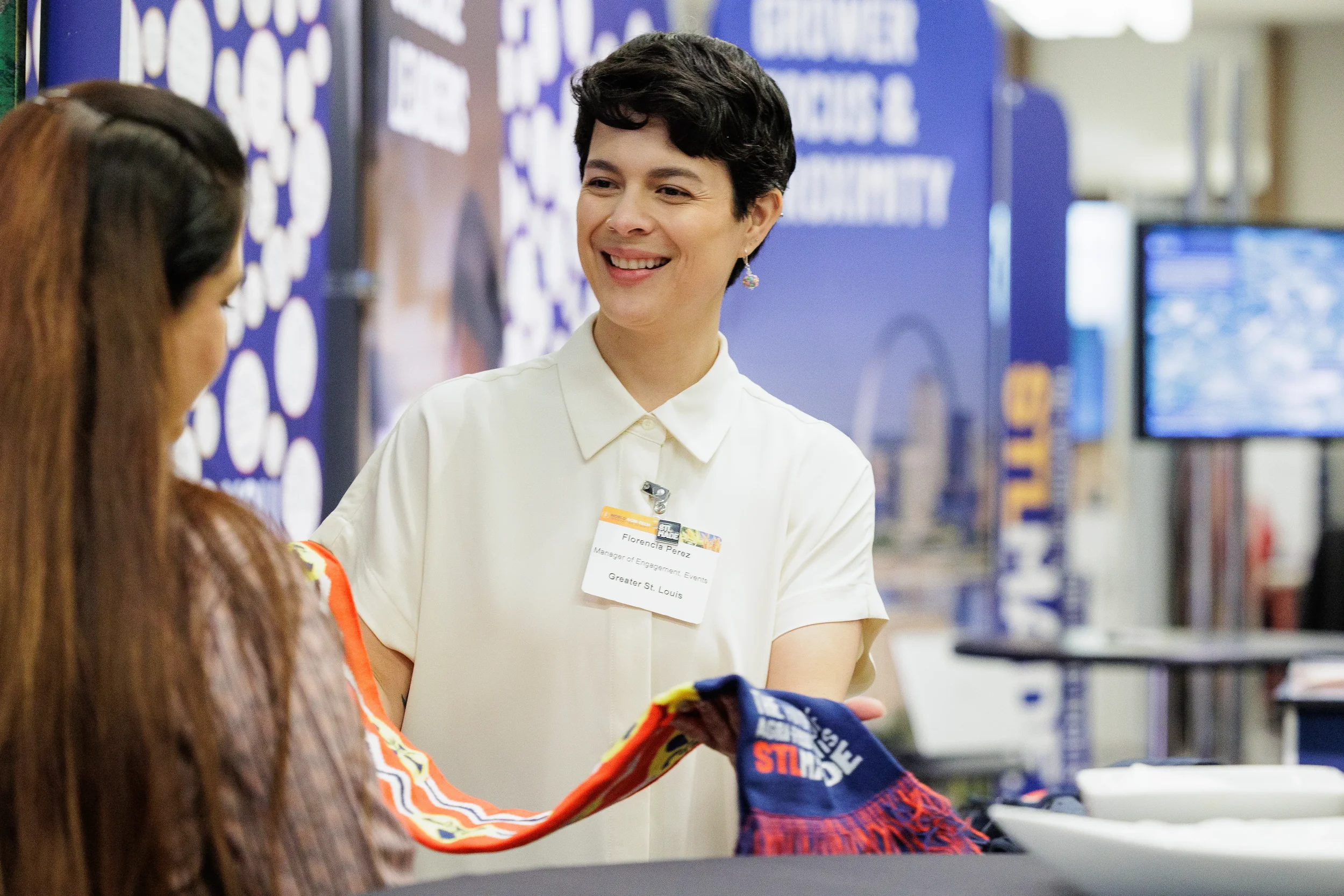 Exhibitor with name badge smiles while engaging attendee at branded booth on Orlando trade show floor