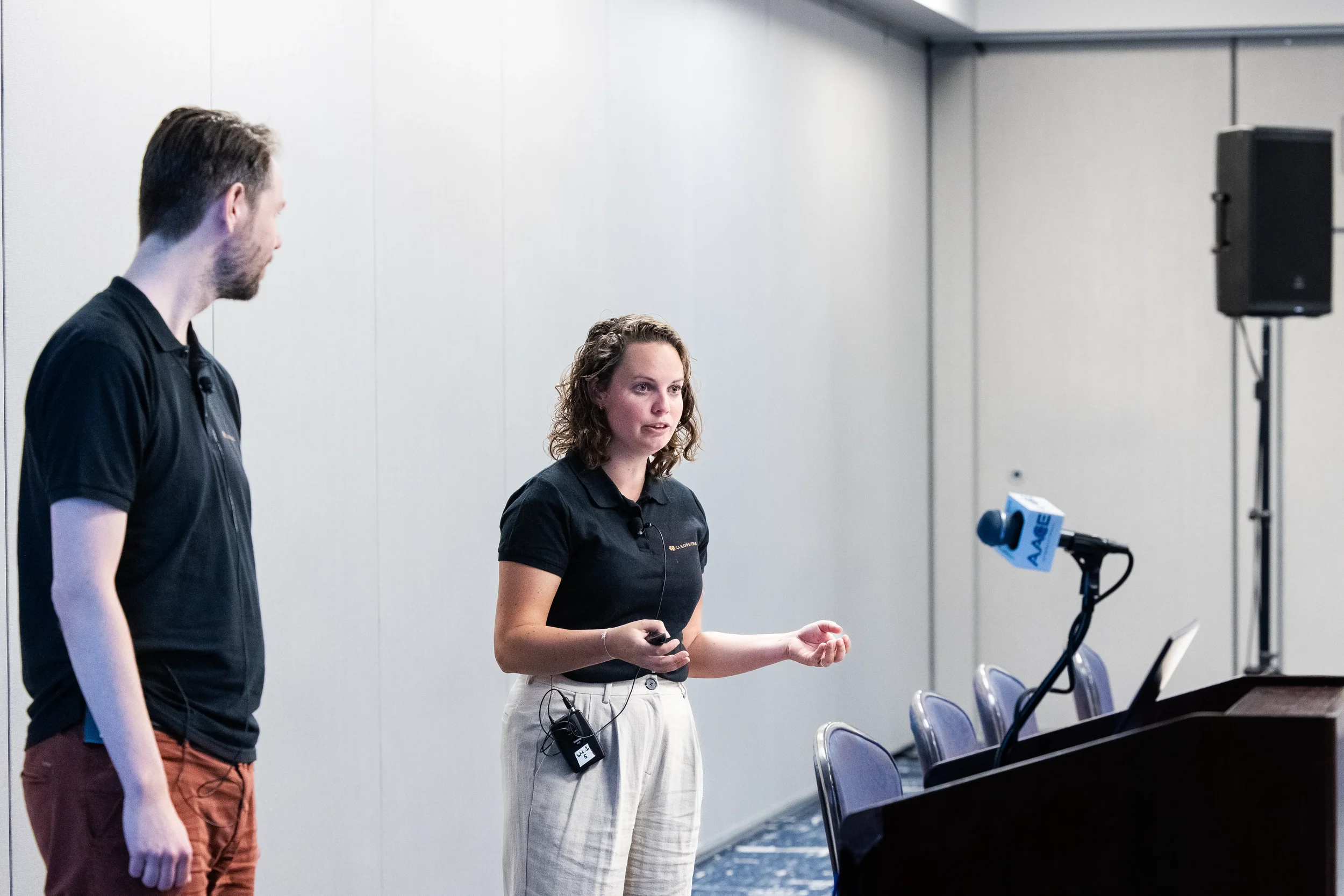 Two presenters discuss during breakout session at Chicago conference with microphone and speaker equipment on stage