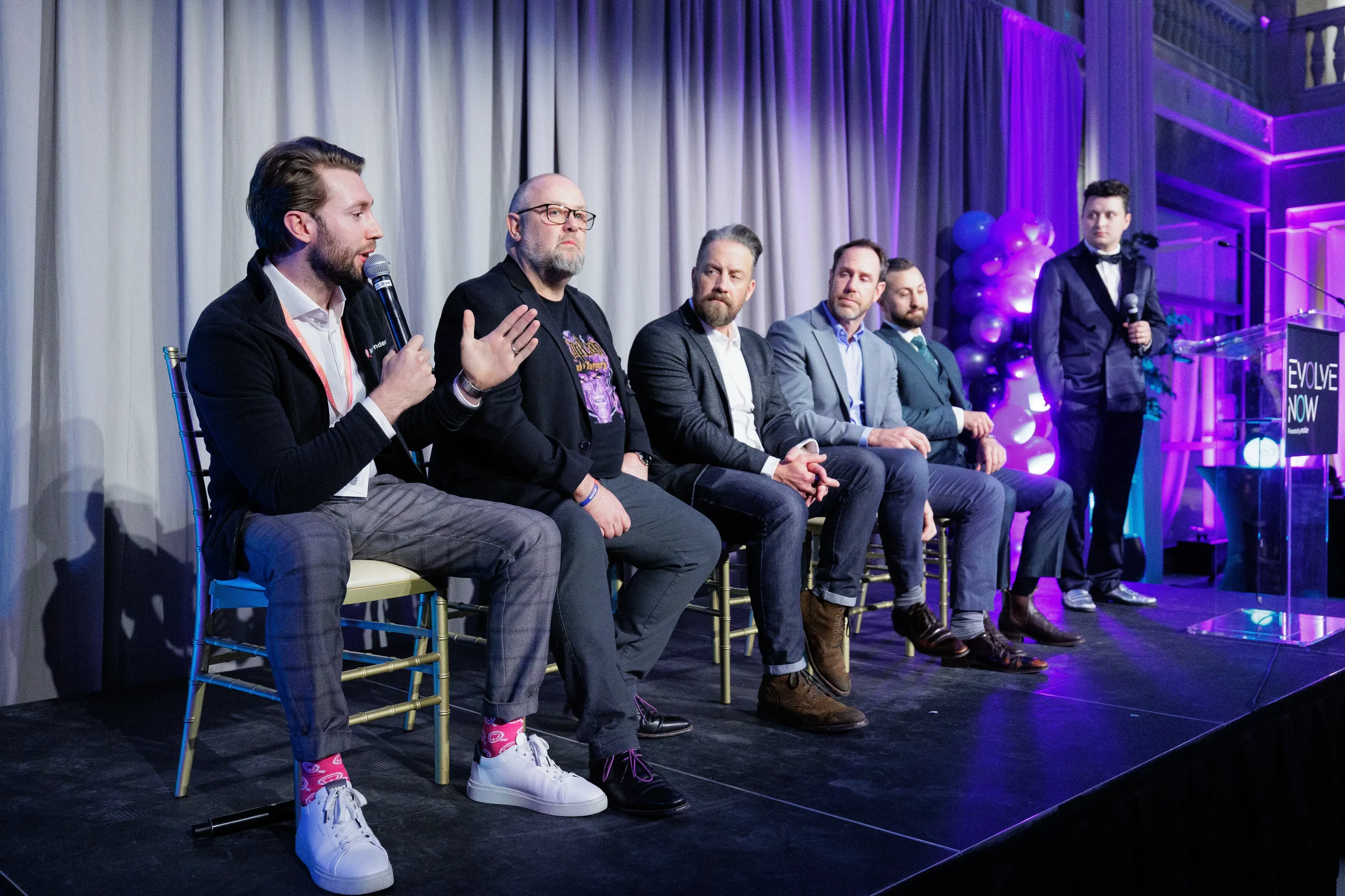 Panelist speaks and gestures while full panel and emcee look on at Chicago industry conference