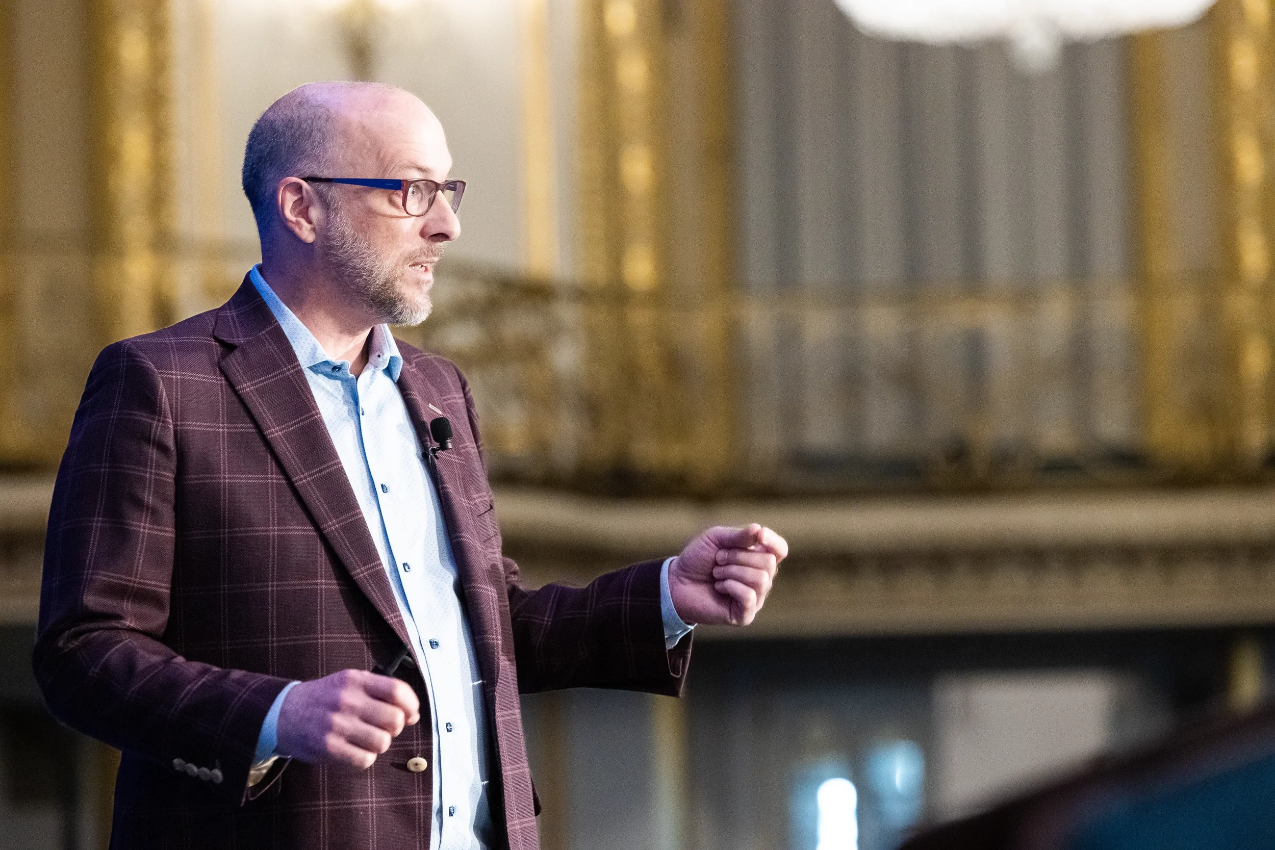 Keynote speaker gesturing on stage in ornate Chicago hotel ballroom