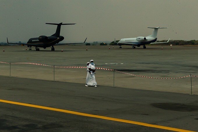 Social Divide 

An early arrival among the reception party dressed in #allwhiteeverything carries a baby on her back as she walks past jet airplanes on the run way observing the red and white guide lines laid out to enforce #COVID19 social distancing