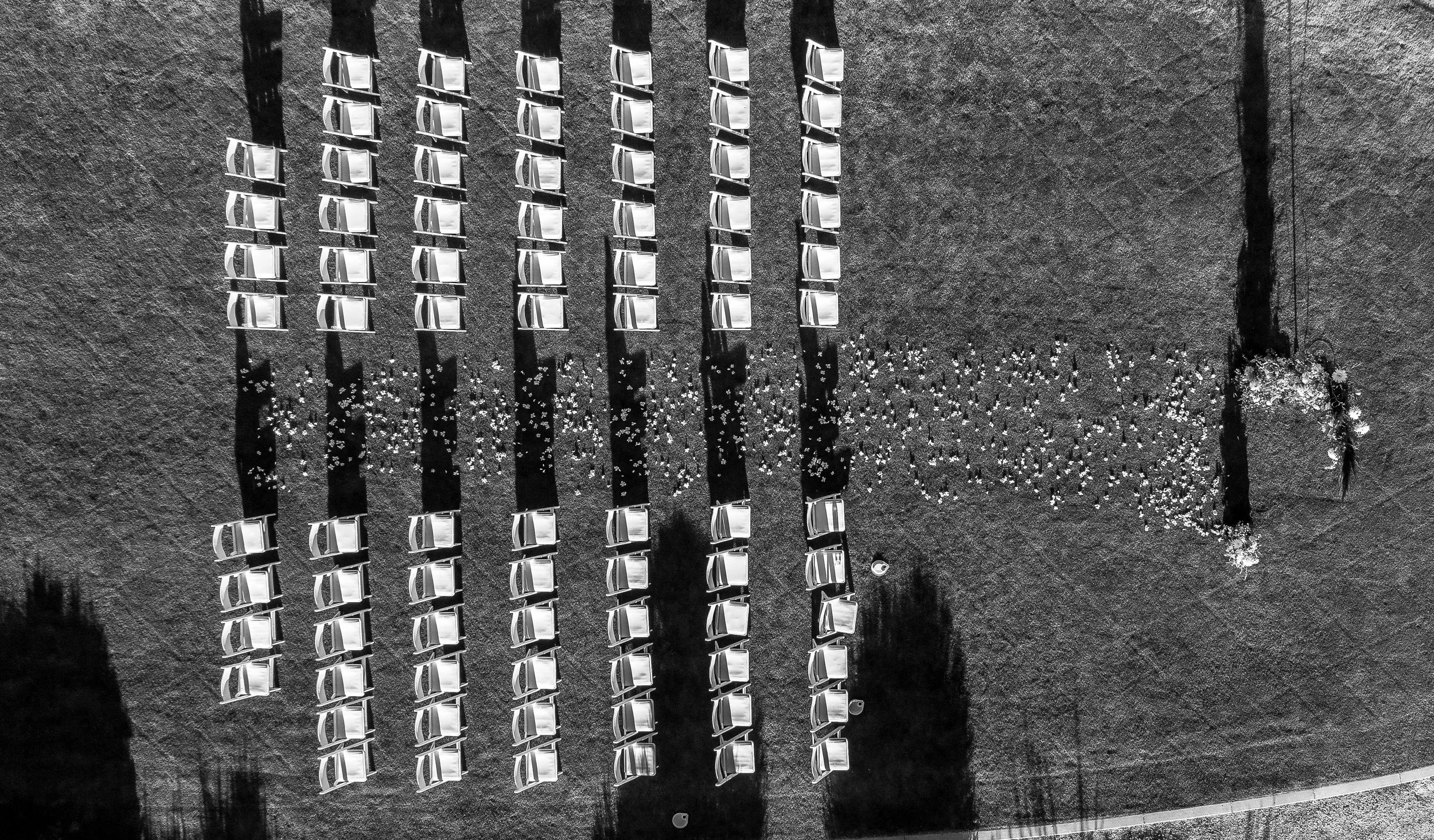 An aerial view of a grassy area with numerous white folding chairs arranged in rows, outdoor and along with a person in white lying on the grass, creating a message that spells out 'say yes.'