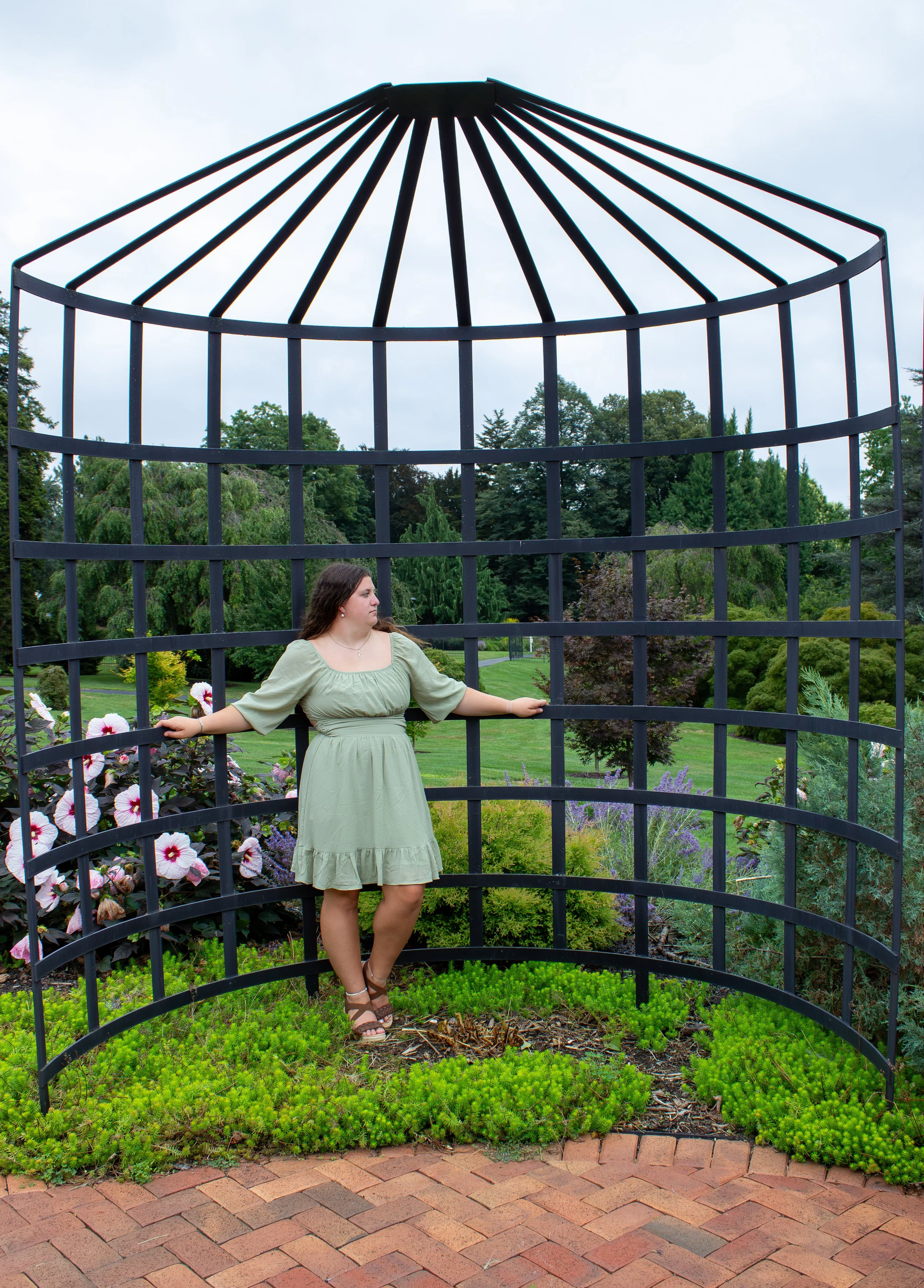 A high school senior girl wearing a green dress standing inside a large decorative metal garden structure during an outdoor session in a Central PA park near Harrisburg.