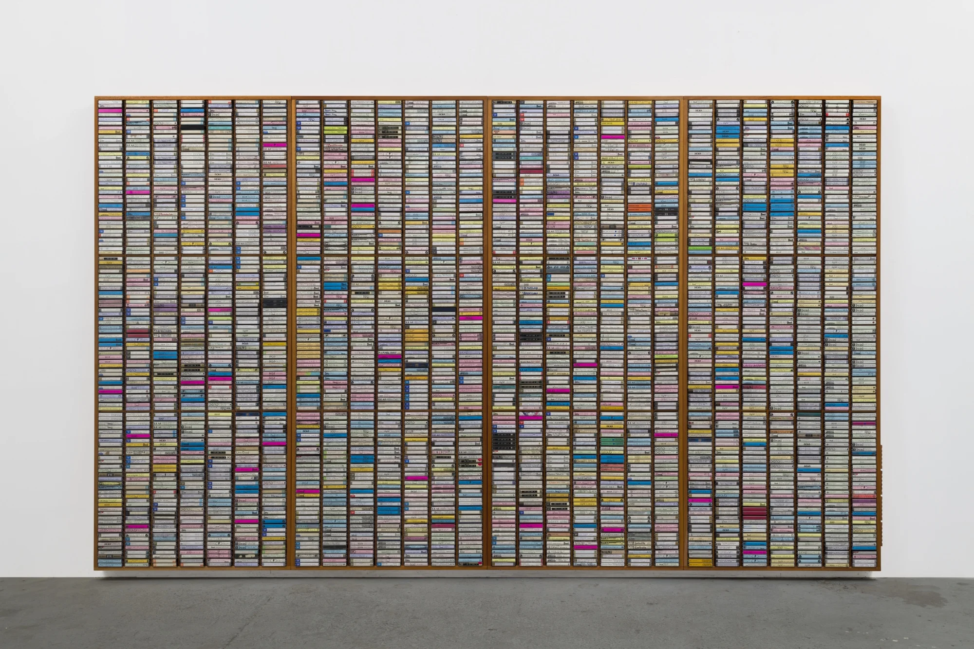 Mark A. Rodriguez, 4th Gen , 2018, custom CNC-routed mahogany and enamel shelving units; audiocassettes; ink and marker on cassette sleeves; plastic cases, 82 ⅞ × 137 ¾ × 3 ½ inches (210.5 × 349.9 × 8.9 cm)