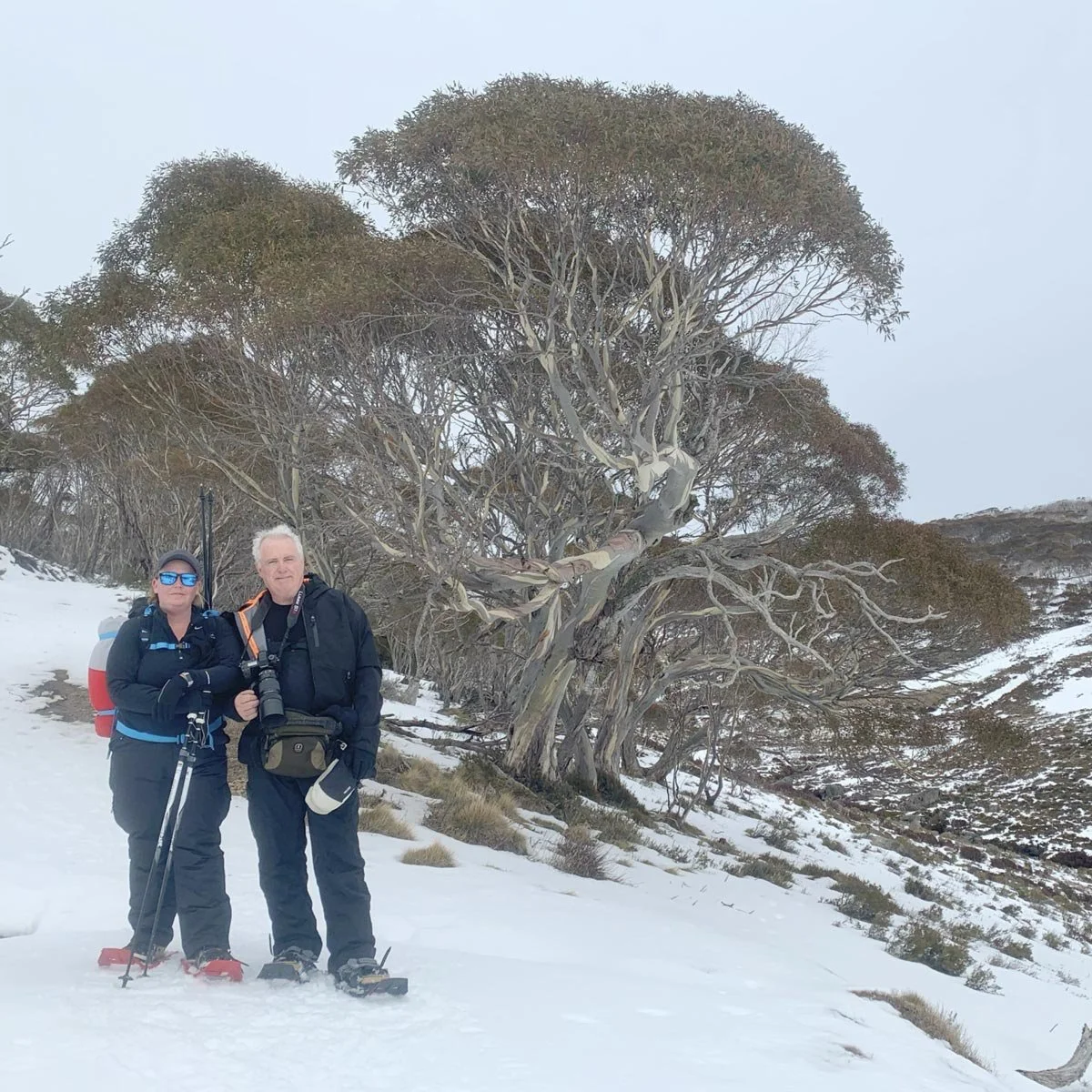 Dani Watson and Ken Duncan standing with camera equipment in a snow-covered alpine landscape