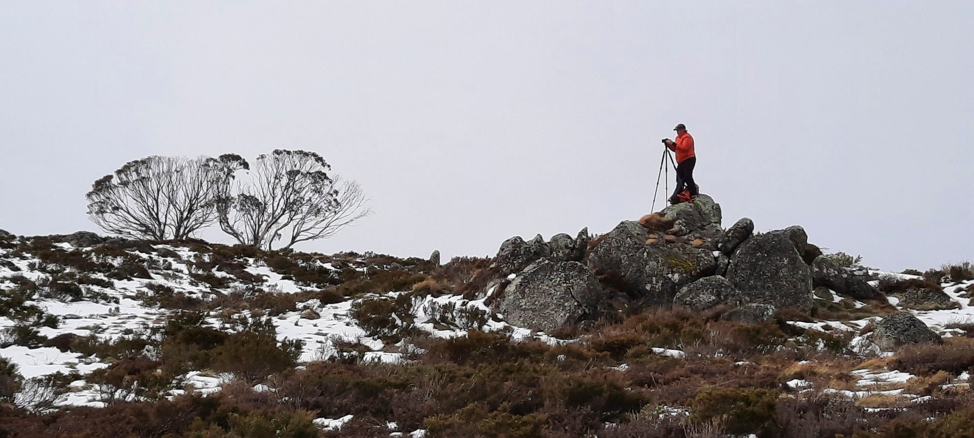 Dani Watson photographing from a granite outcrop above snow-dusted alpine country