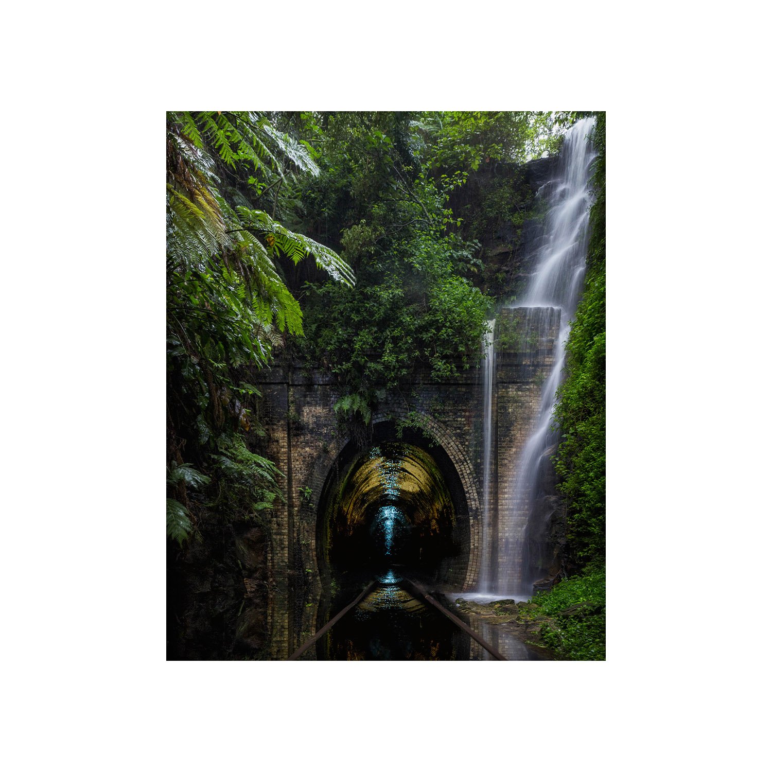 Waterfall cascading over a tunnel surrounded by lush greenery