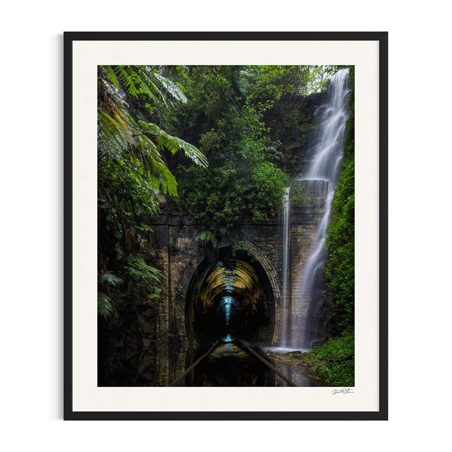 Waterfall cascading over a tunnel surrounded by lush greenery in black frame