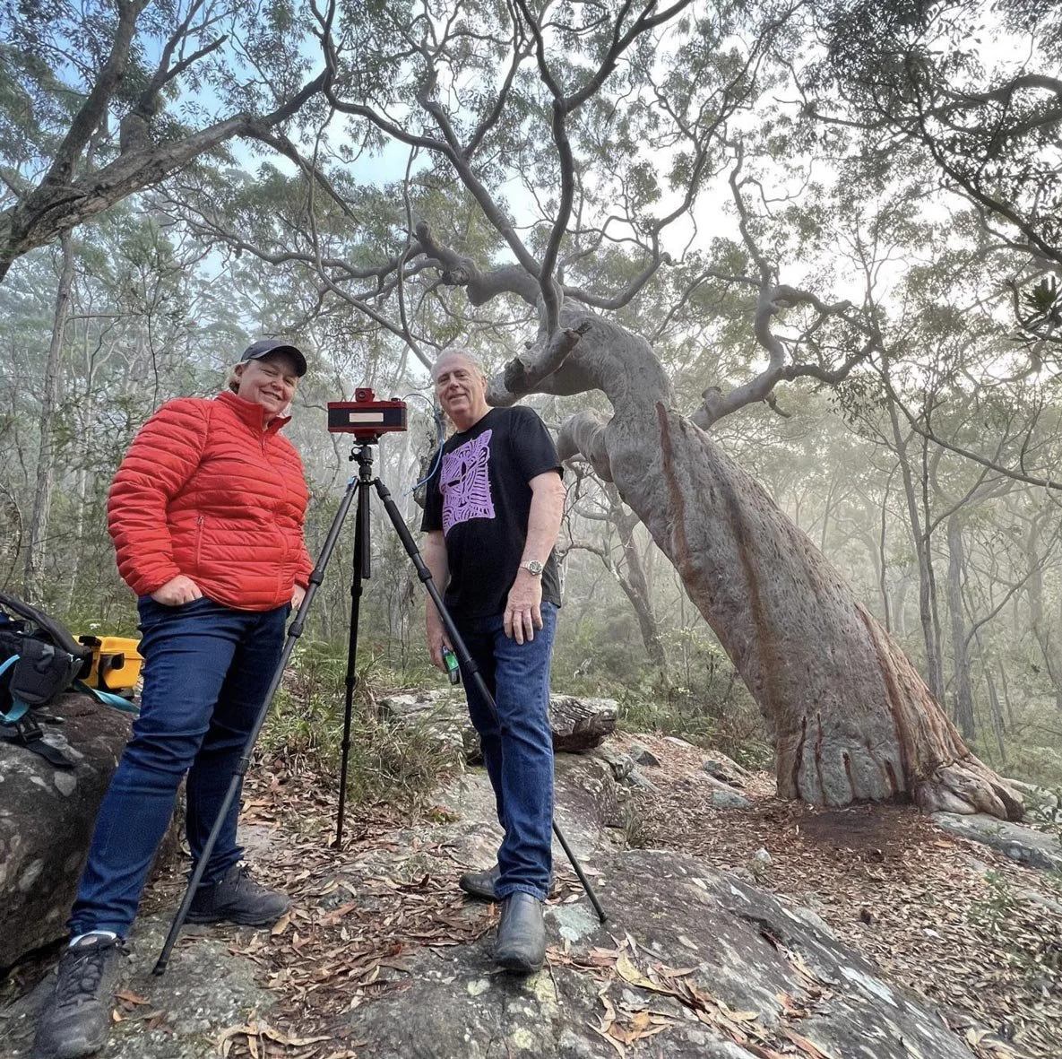 Dani Watson and Ken Duncan beside a Linhof Technorama 617 camera in misty bushland