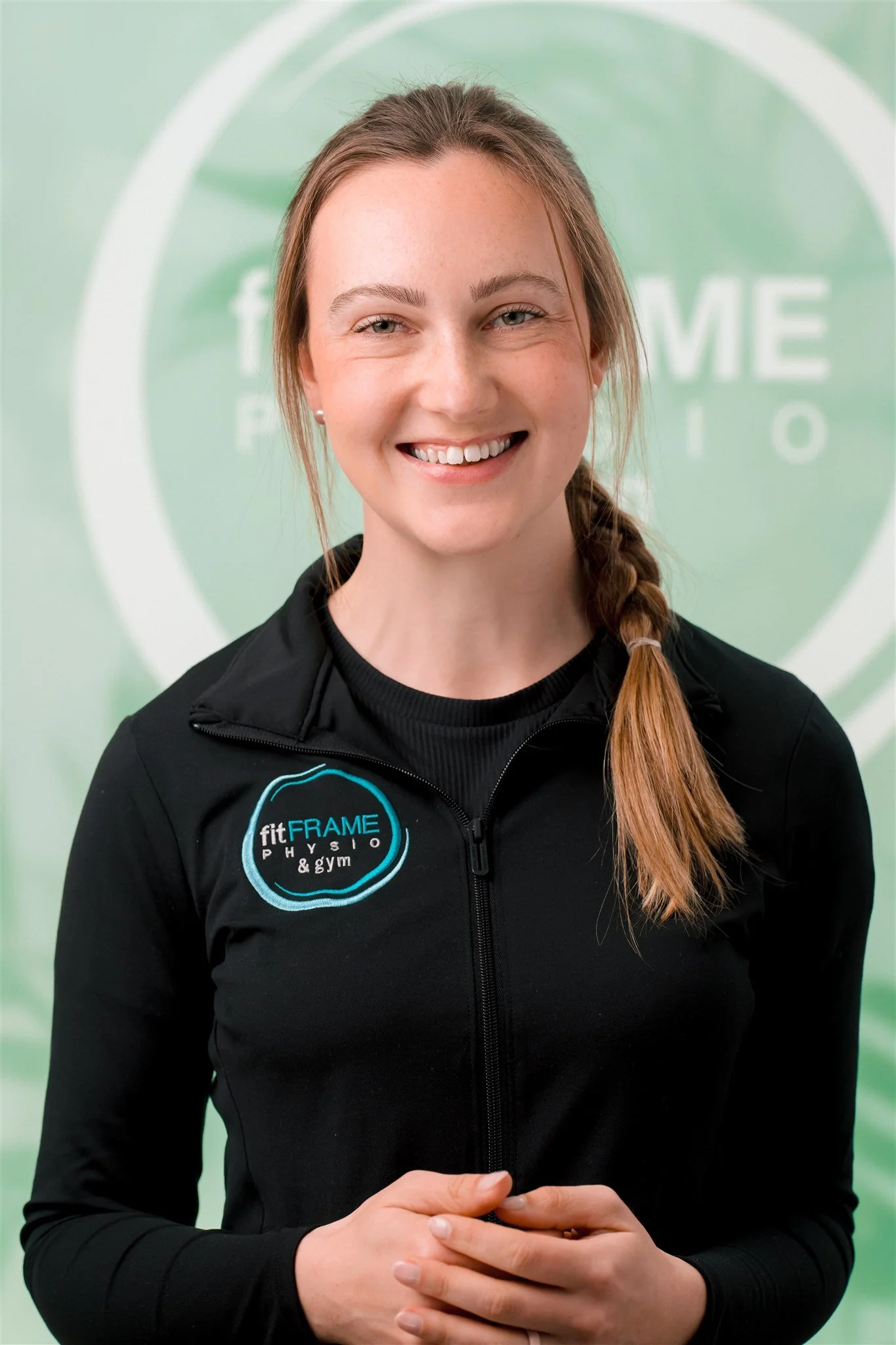 A young woman with light skin, freckles, and blue eyes smiling, wearing a white collared shirt, standing against a light green background.