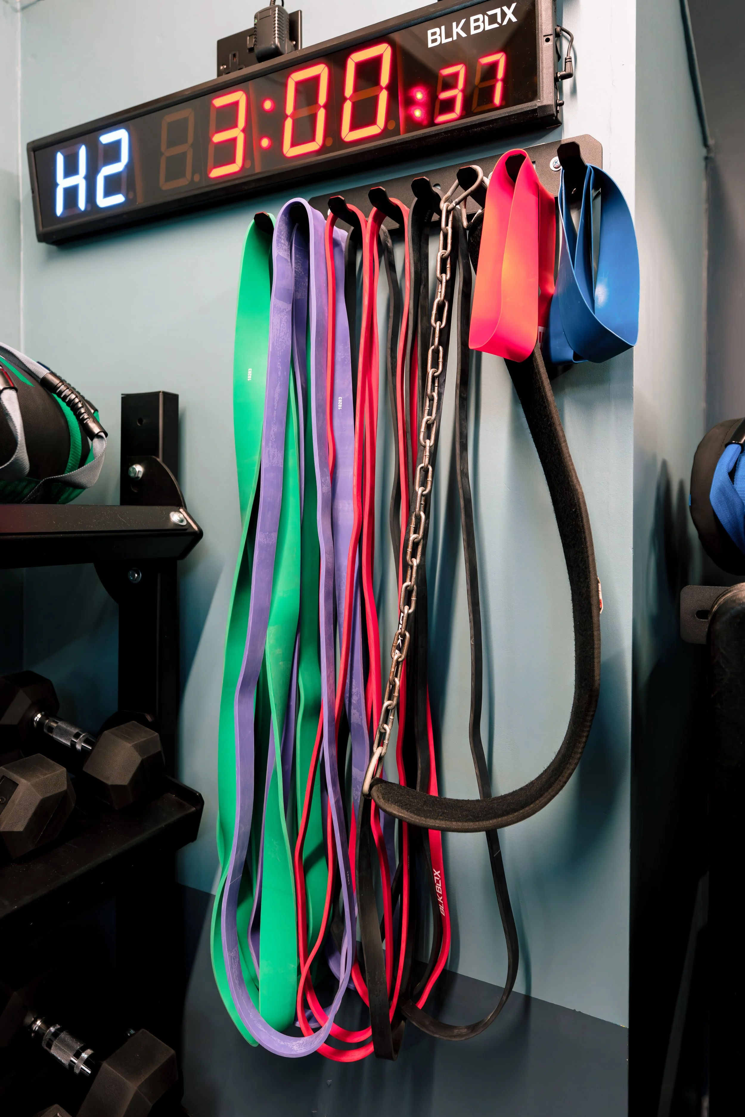 Wall-mounted digital timer and a variety of resistance bands and exercise straps hanging on hooks in a gym.