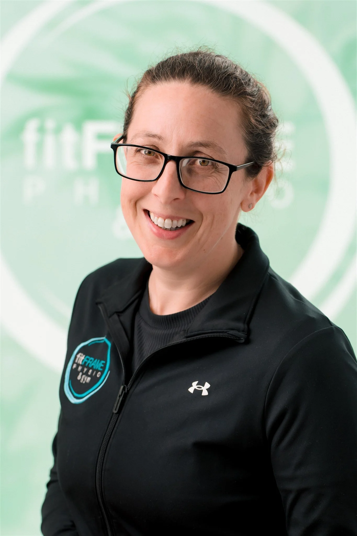 A woman with brown hair in a braid wearing a black "Best Version" t-shirt standing in a gym with exercise machines and colorful posters in the background.