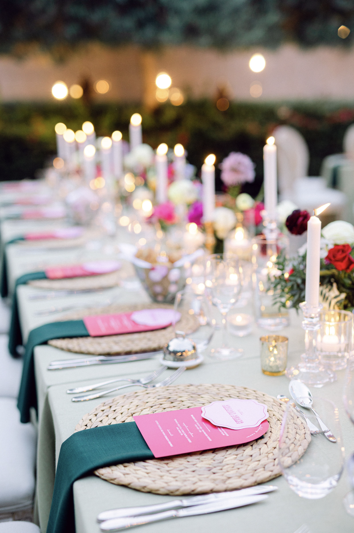 A decorated outdoor dining table with candles, flowers, and place settings, set for an event during the evening.