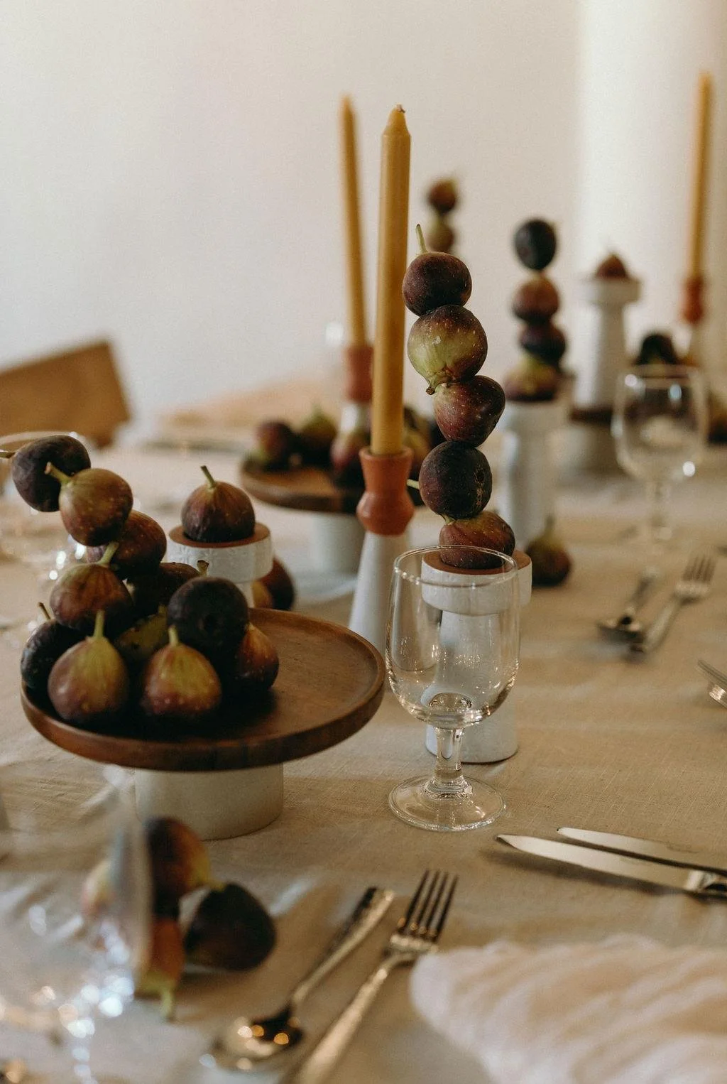 A table set with fig fruit decorations, candles, and glassware for a formal dining setting.