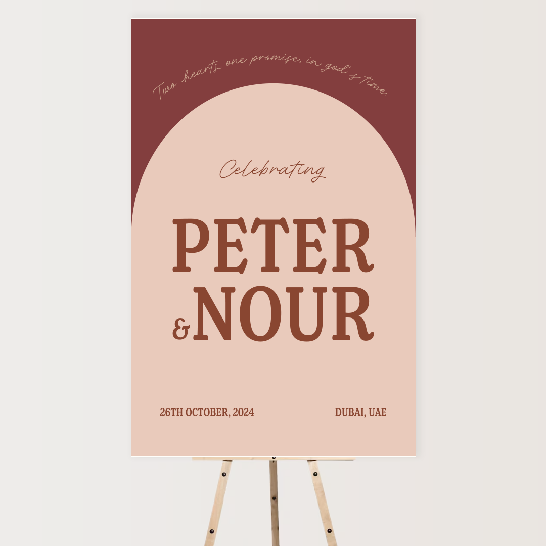 A wedding or celebration event poster on a wooden stand with pink and brown colors. The text reads 'Celebrating Peter & Nour, 26th October 2024, Dubai, UAE' with a quote at the top, 'Two hearts one promise, in God I trust me.'
