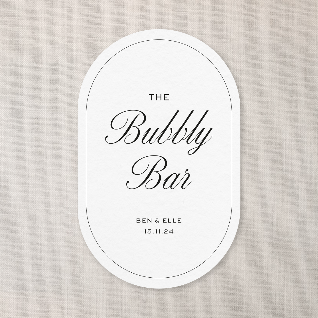 A white oval sign with black cursive text that says "The Bubble Bar," along with smaller text reading "Ben & Elle" and the date "15.11.24." The sign is on a light beige textured background.