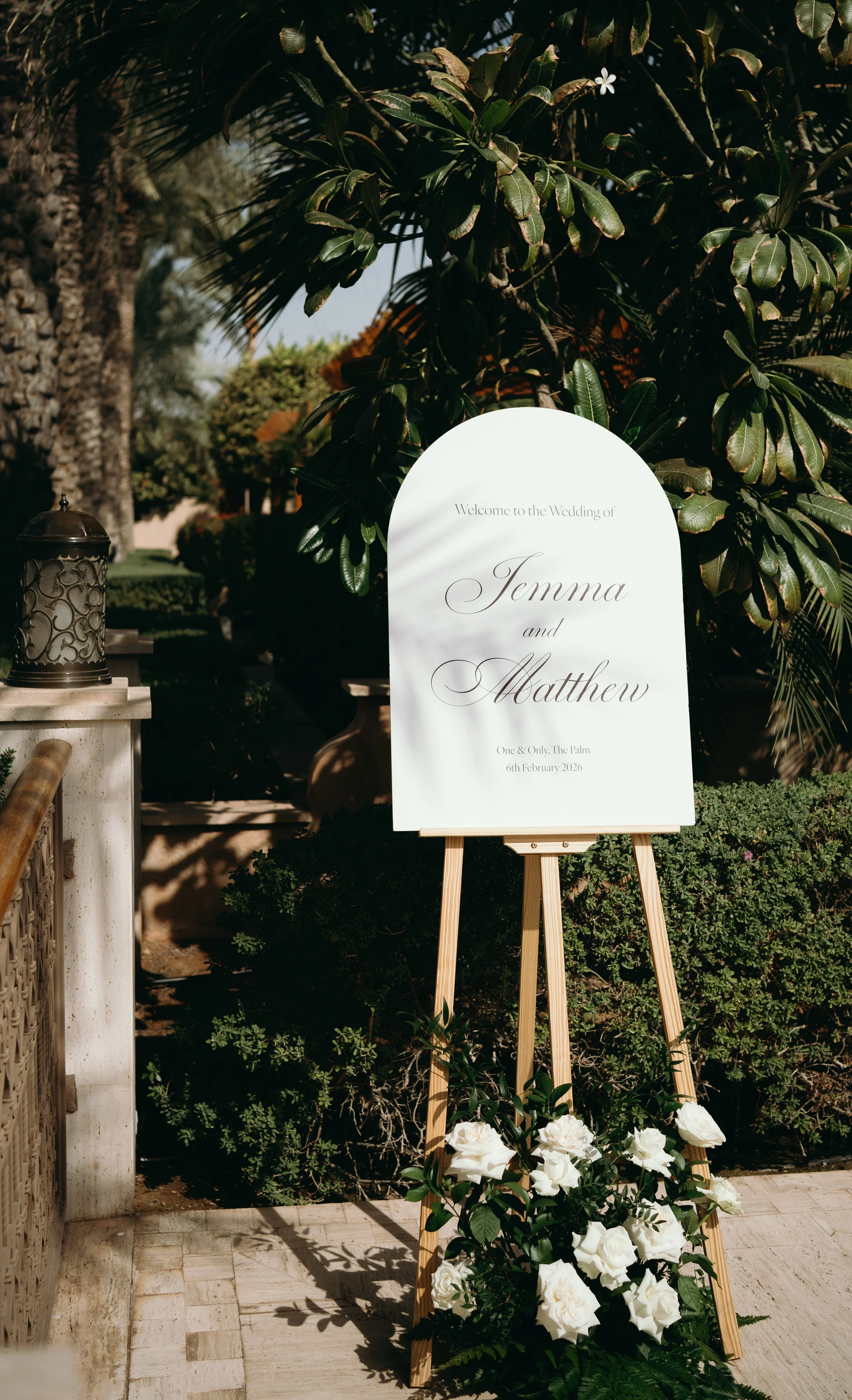 Wedding welcome sign with white roses at a lush outdoor garden venue.