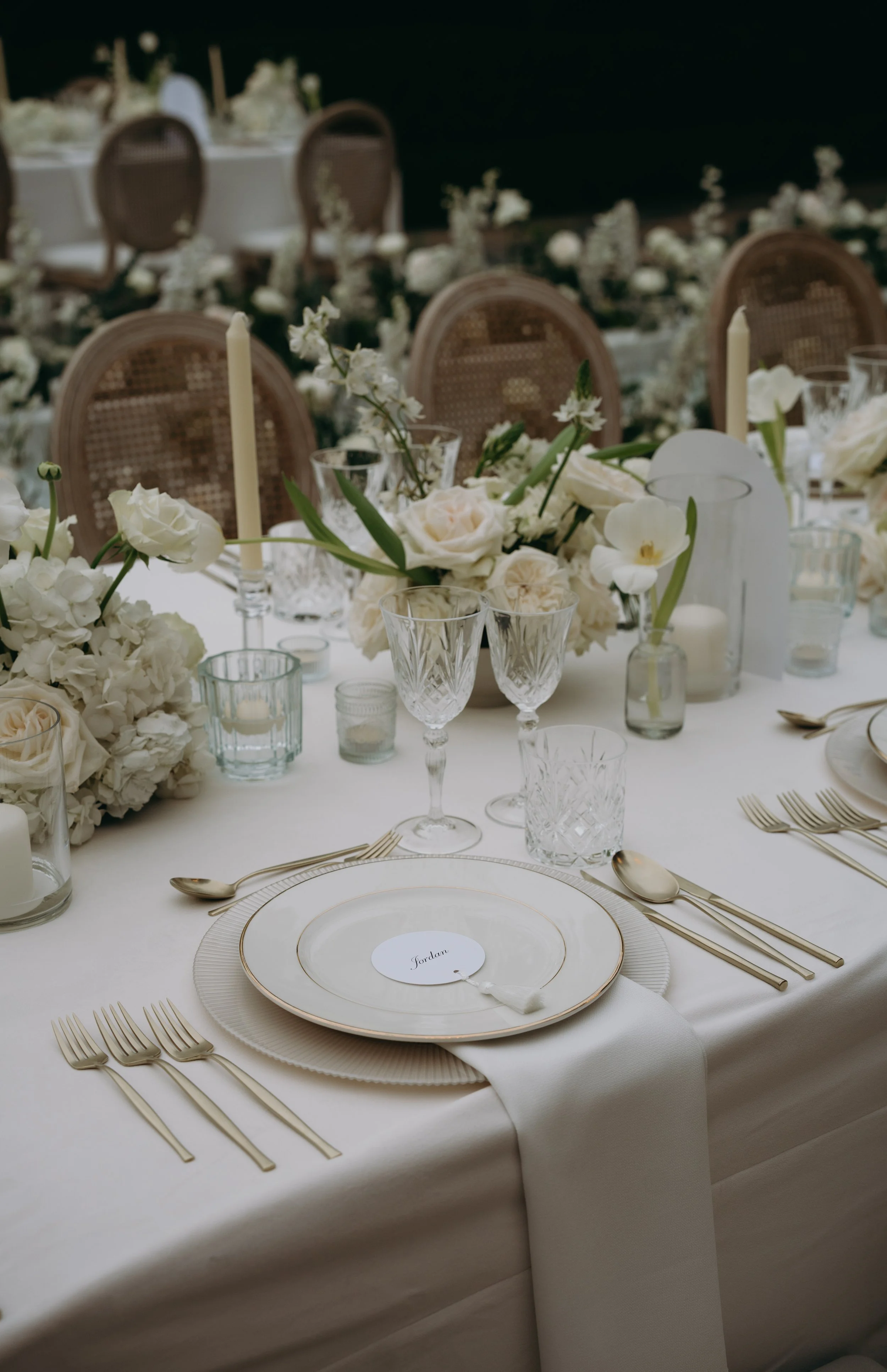 Elegant banquet table decorated with white flowers, candles, and glassware, set for a formal event or wedding reception.