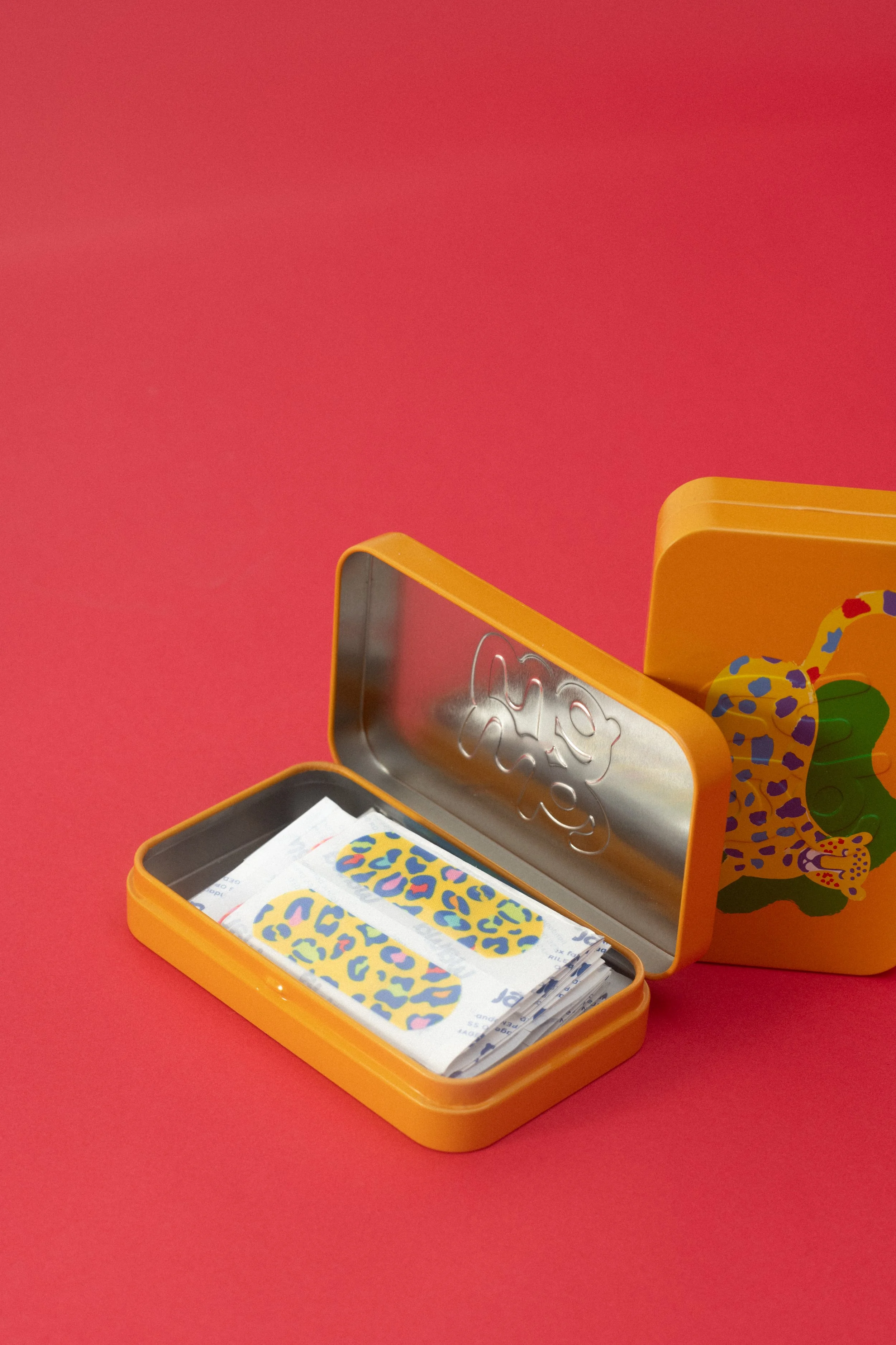 An orange metal box containing stickers with colorful, leopard print design, placed on a bright red surface against a red background.