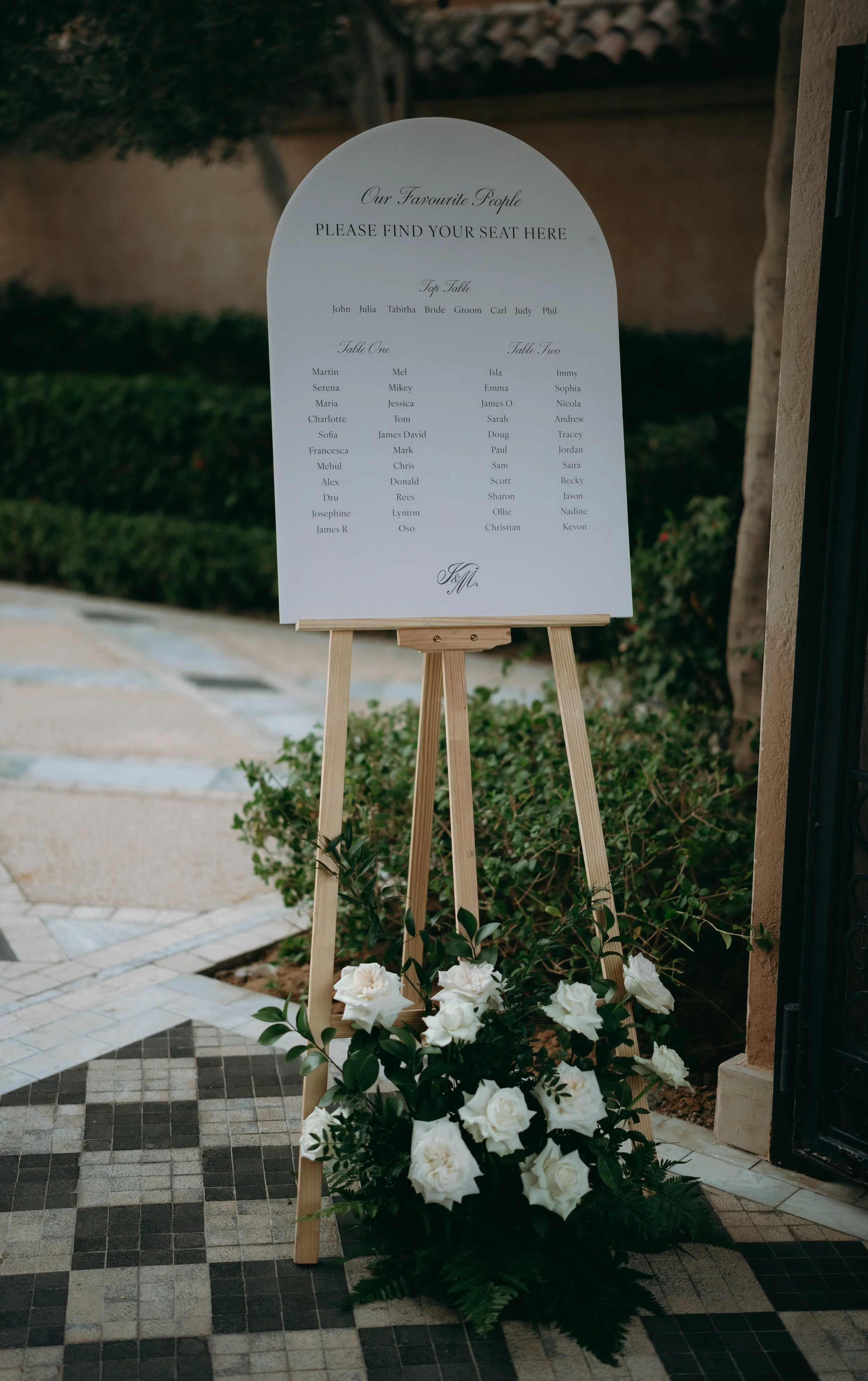 Wedding seating sign on a stand with white roses at the base, announcing reserved seats for friends and family at an outdoor wedding.