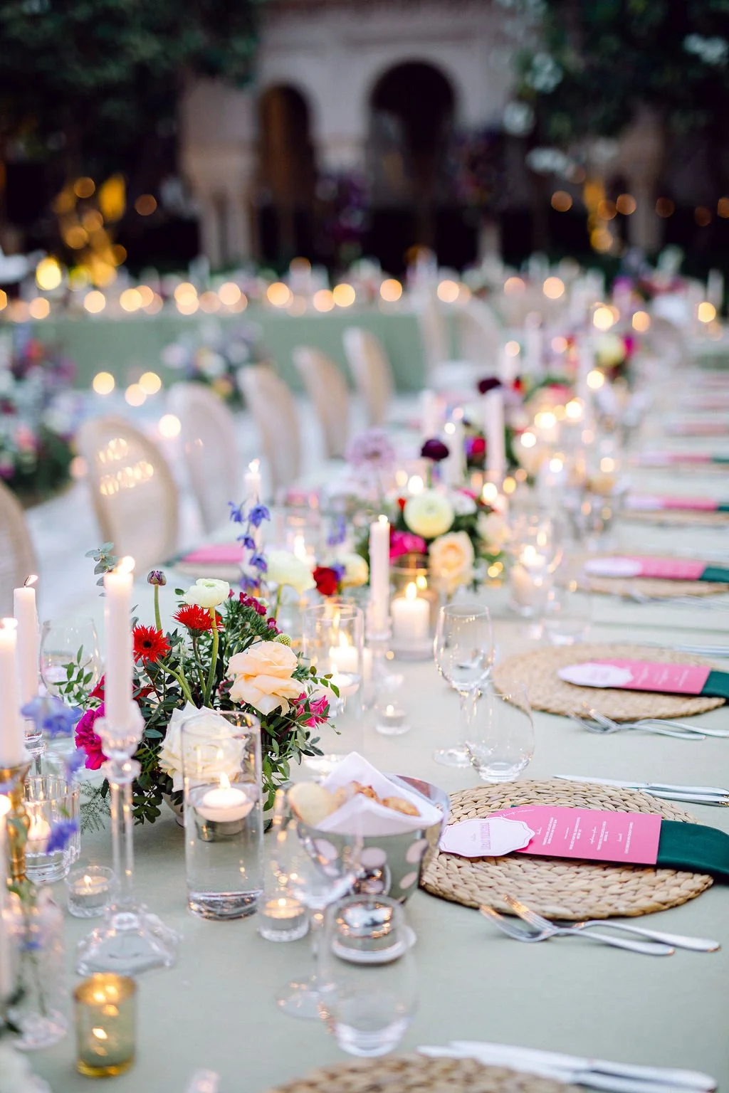Elegant outdoor dining table decorated with floral arrangements, candles, and table settings for a celebration or event.