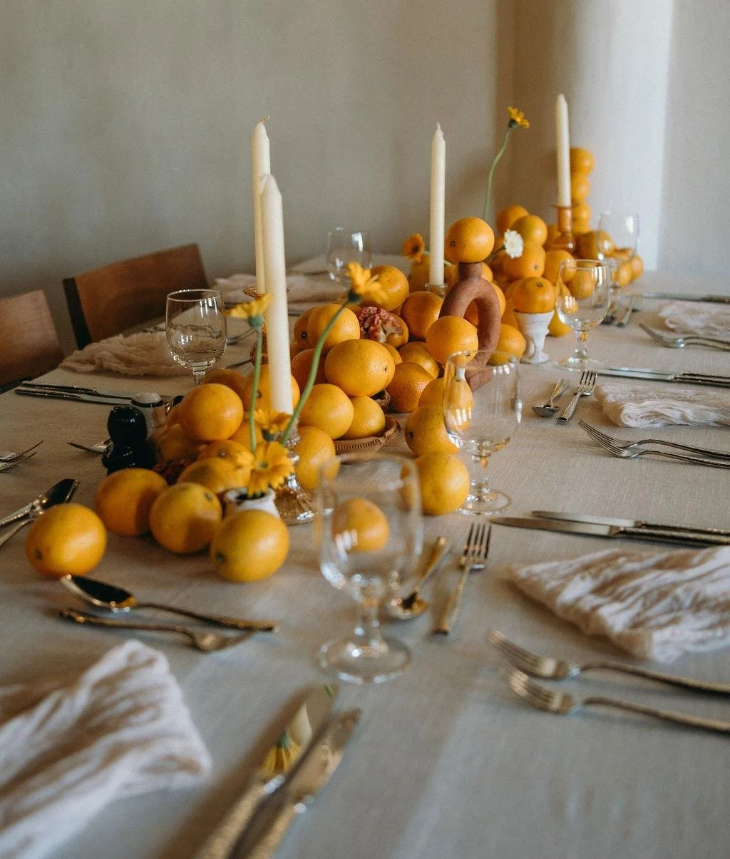 A table set for a meal with a centerpiece of oranges, white candles, and flowers.