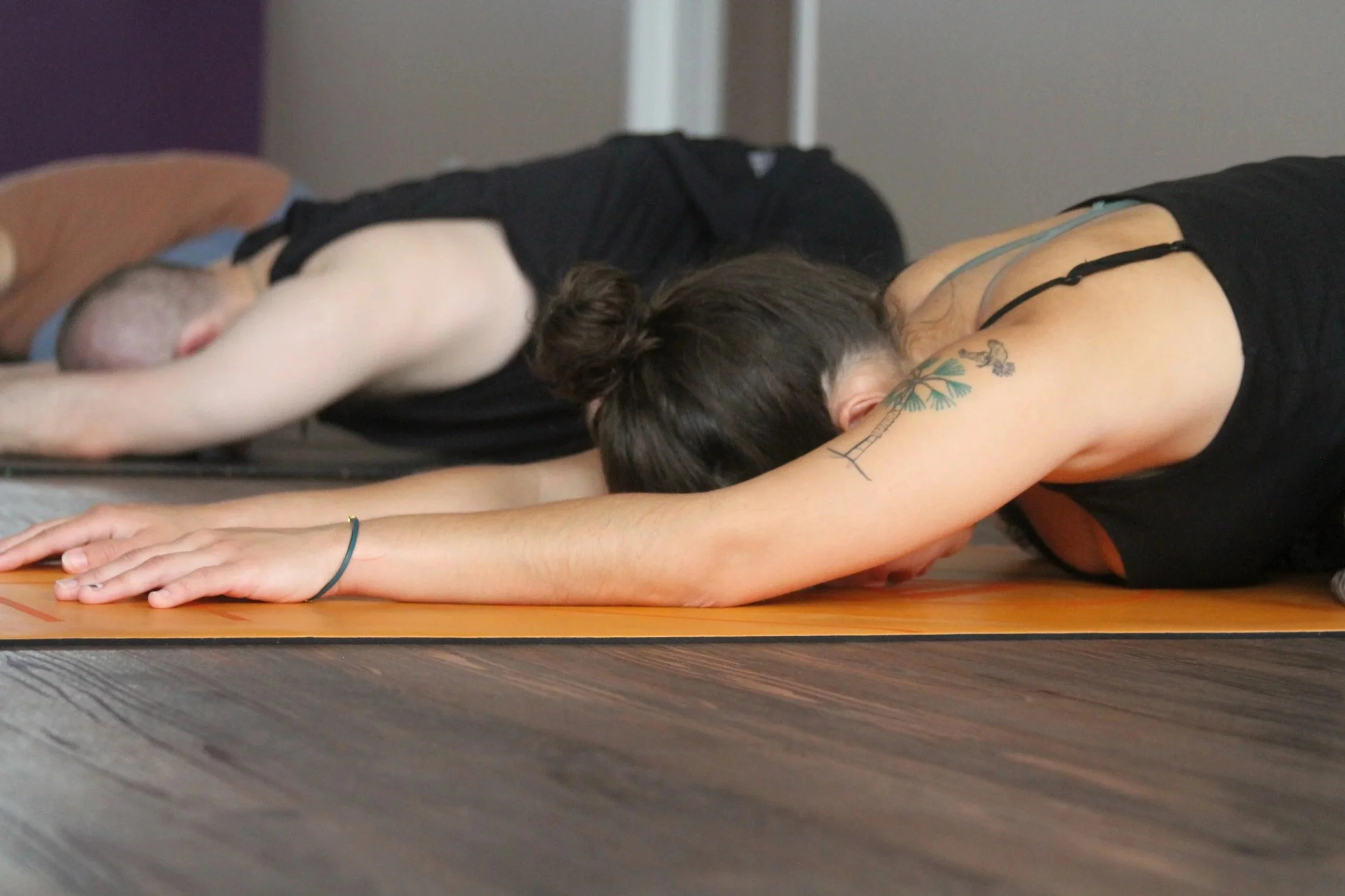 A woman with tattoos on her arm practicing yoga in child's pose on a yoga mat.