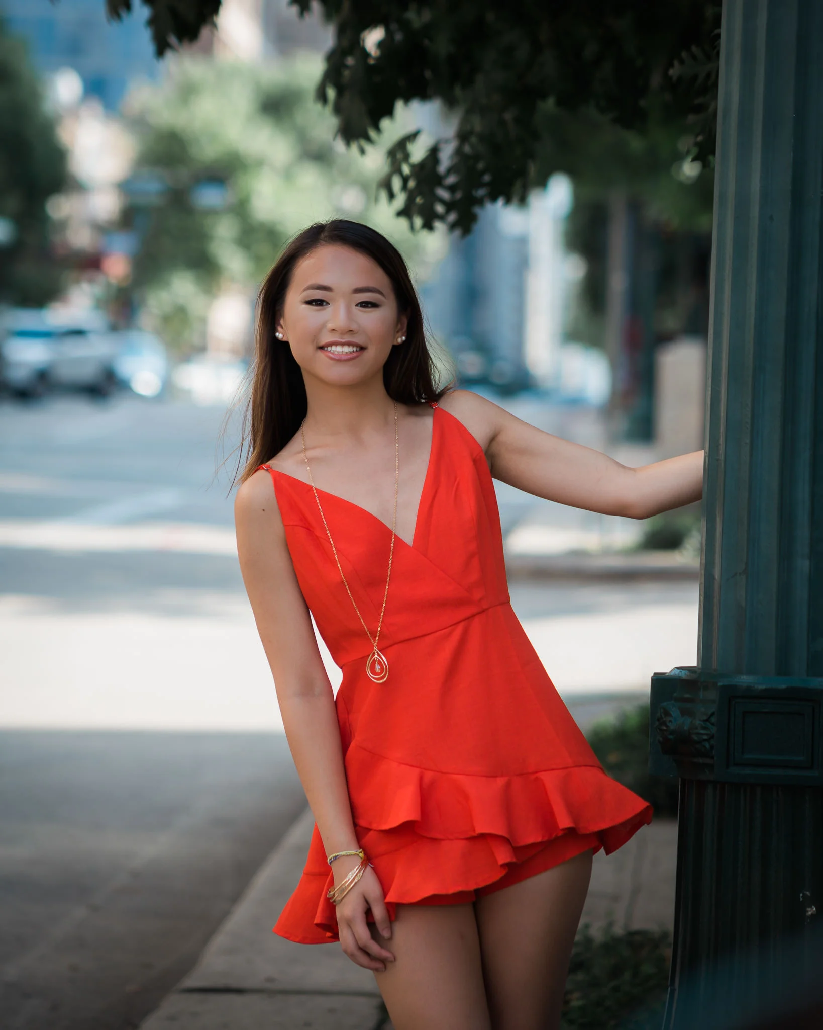Senior girl in red dress swinging from lightpole
