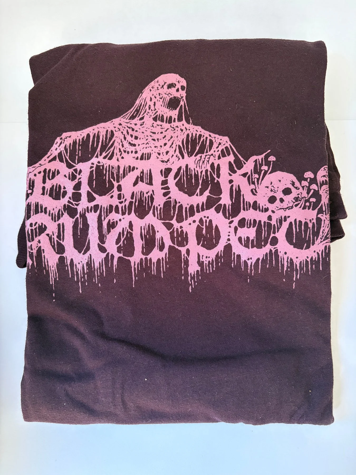 This folded cotton t-shirt depicts a mycelium-covered skeleton and skull printed in mauve ink on oxblood fabric.