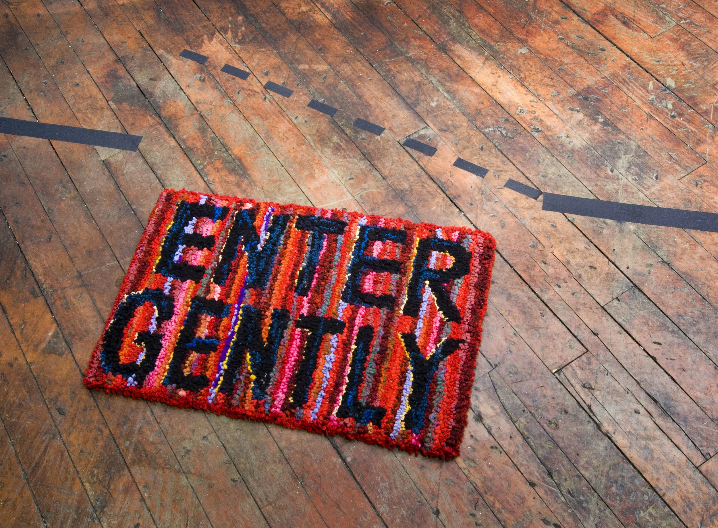 Situation Uncontainable by Architecture . hand hooked wool rug, tape. dimensions variable, 2006. In response to architect Eileen Grey’s house E.1027, where “entrez lentement” (enter slowly) is stenciled on the wall, this piece relies on flexible structures whose meaning is constituted in the moment of use. The text on the welcome mat refers both to a sexual move and a spatial move. The incongruity between the physical presence of the rug and the speculative representation of the tape drawing is confusing. Where is the location of what event?