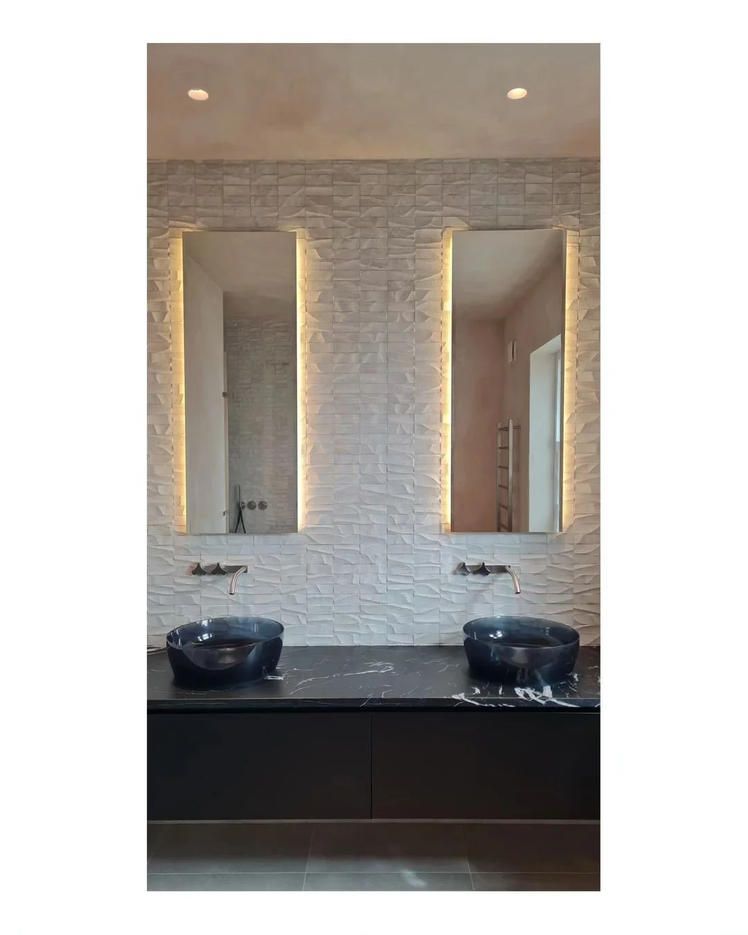 View of the Master Ensuite in our recently completed project in Barnes, London UK. A full height textured tile is the backdrop to the transparent cristalmood bowls that seat on a honed nero marquinia marble worktop and matching colour wall hung vanit