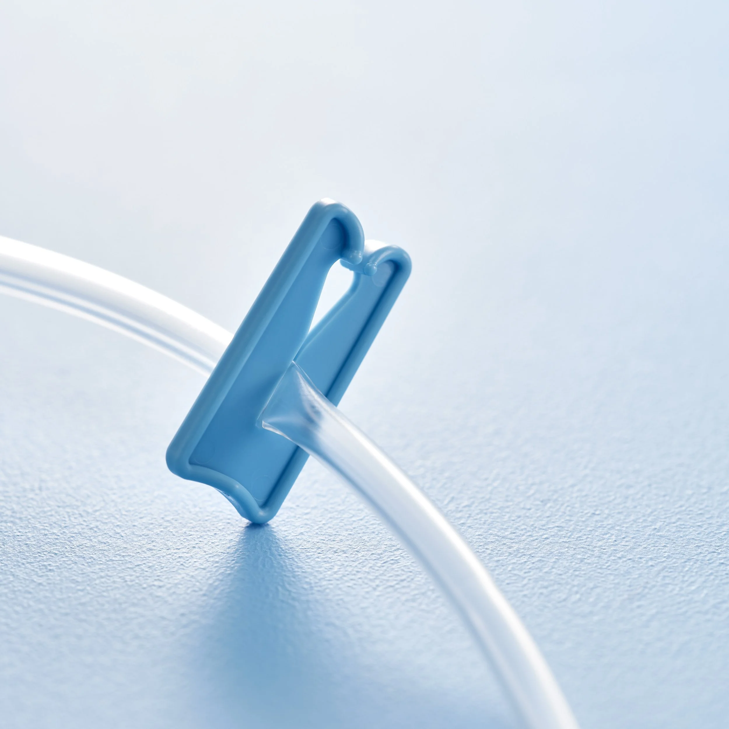 Close-up of a blue medical connector attached to a clear tube on a light blue surface.