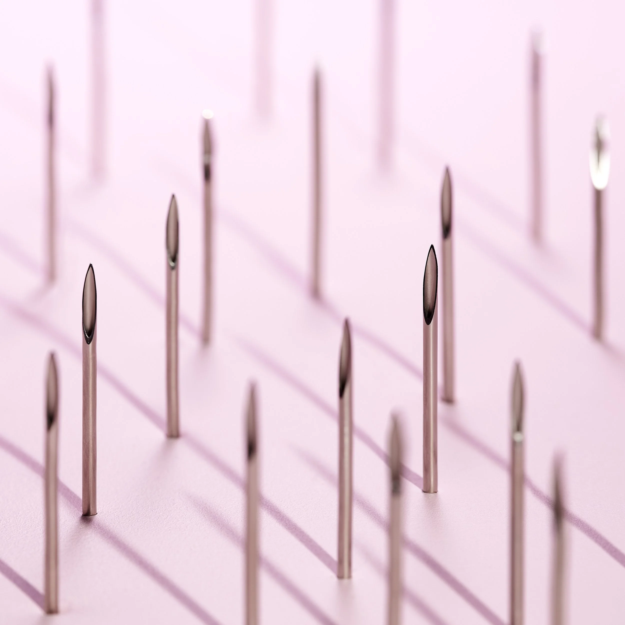 Close-up of multiple pink and black dental curing light tips standing upright on a pink surface, with shadows cast behind them.