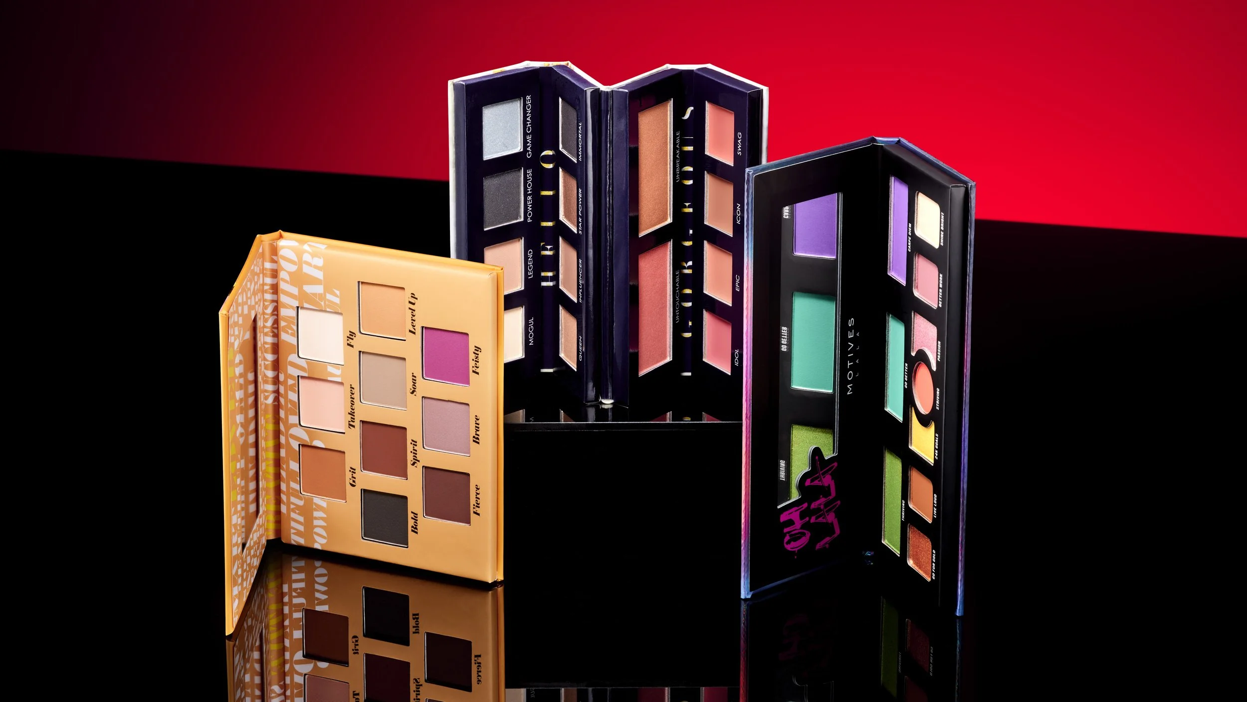 Four colorful eyeshadow palettes with various shades, displayed on a glossy black surface with a red and black background.