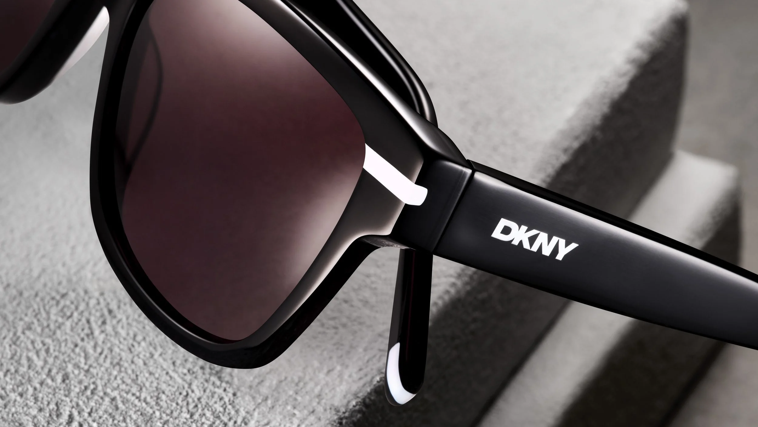 Close-up of black DKNY sunglasses with pink-tinted lenses resting on a light gray textured surface.