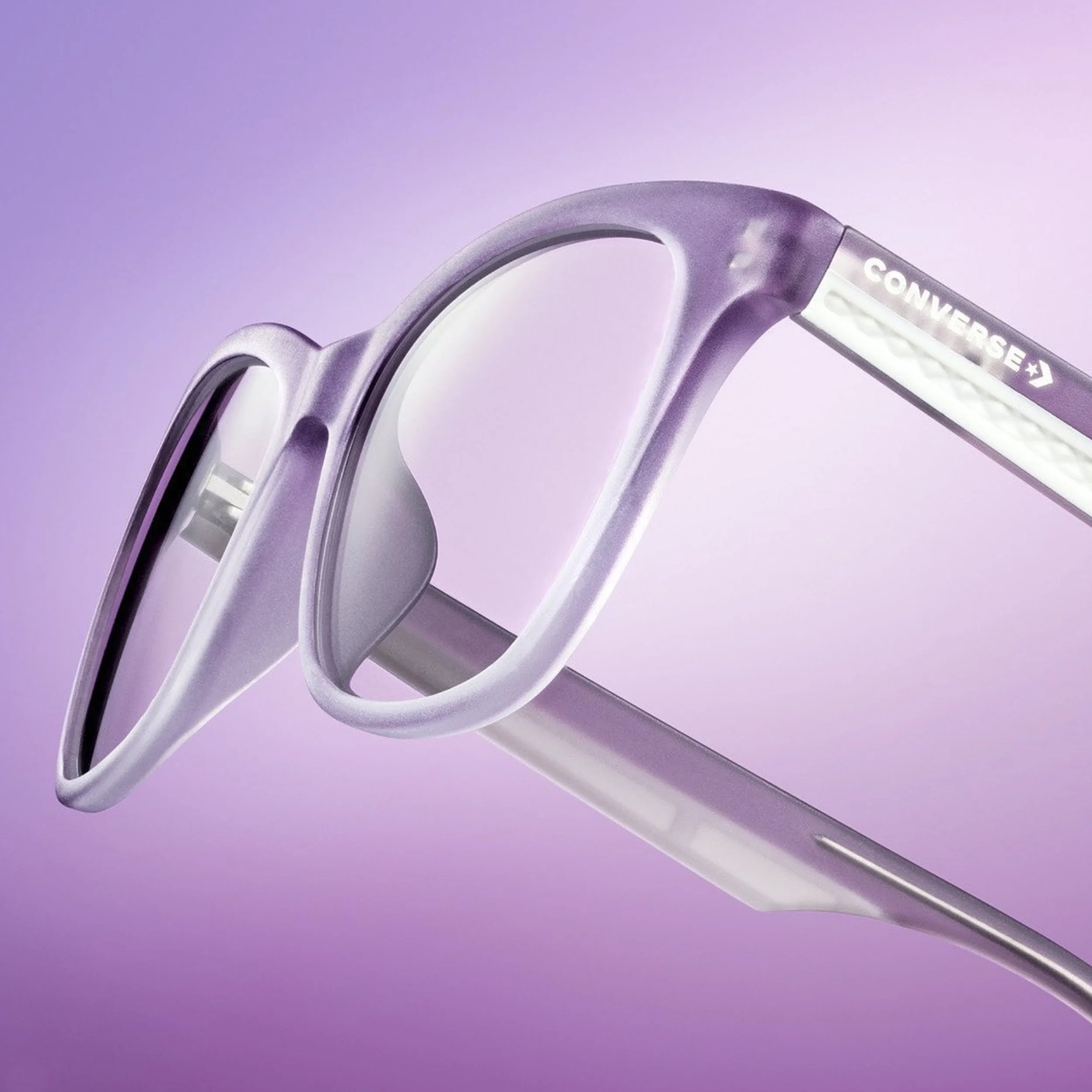 Close-up of purple and white Converse-branded eyeglasses against a pink gradient background.