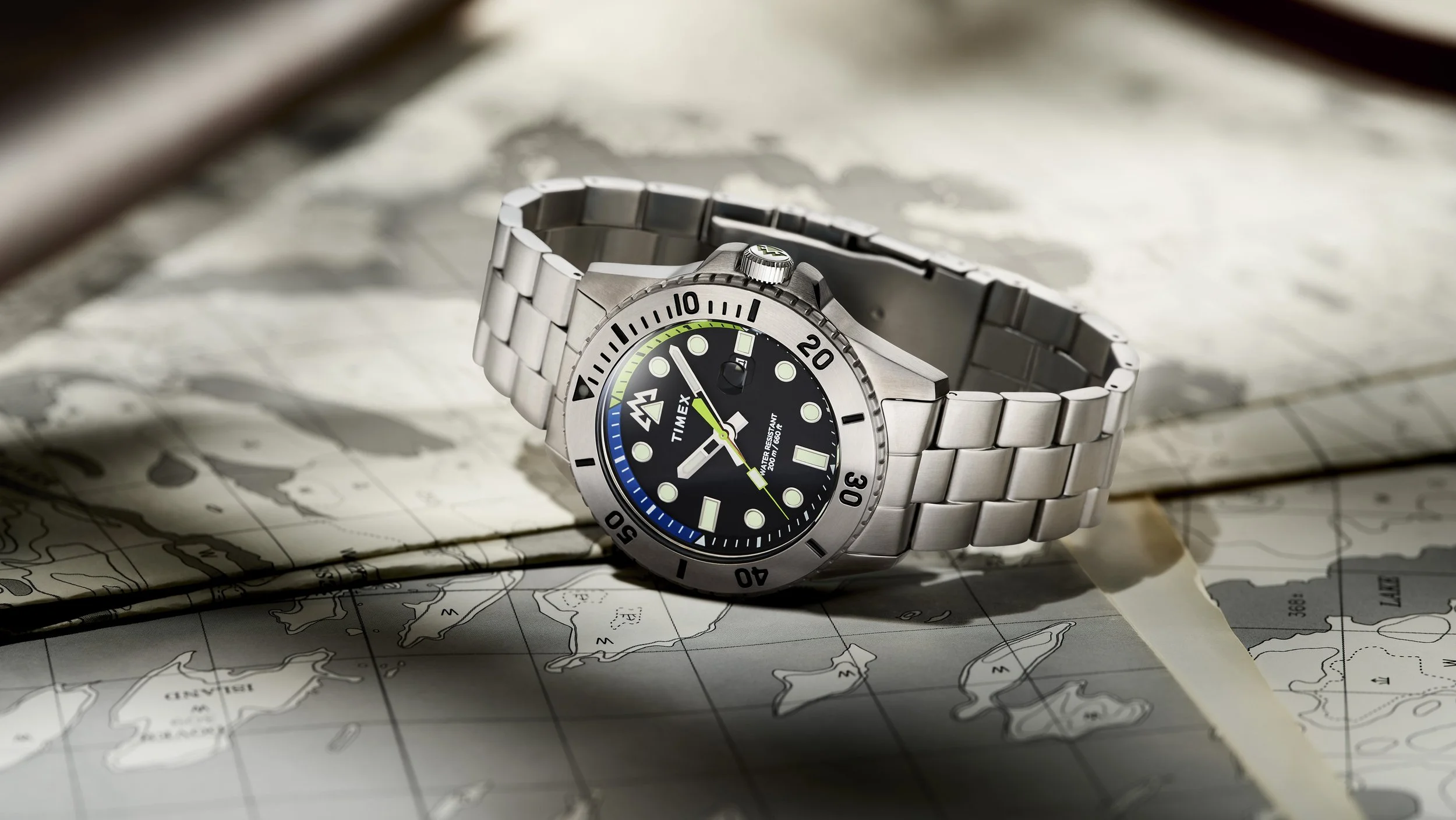 A silver Timex wristwatch with a black dial, luminescent markers, and a rotating bezel, resting on an open nautical map.