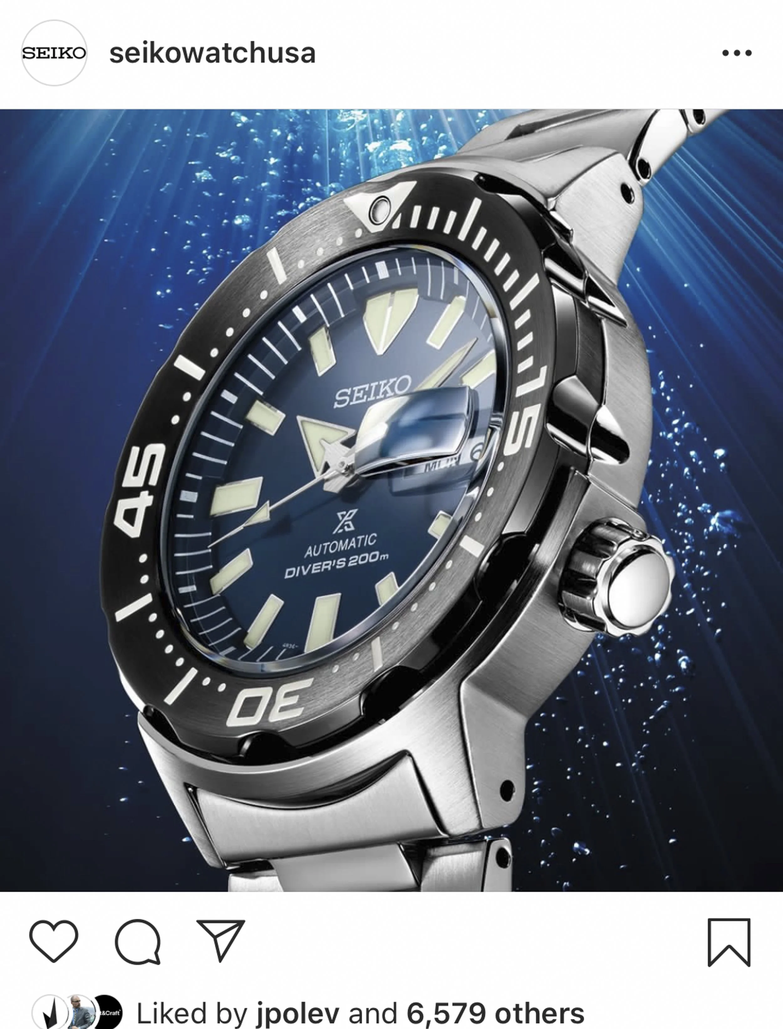 A Seiko dive watch submerged underwater, displaying a blue face, luminous hands and markers, a date window with magnifier, rotating bezel, and stainless steel band.