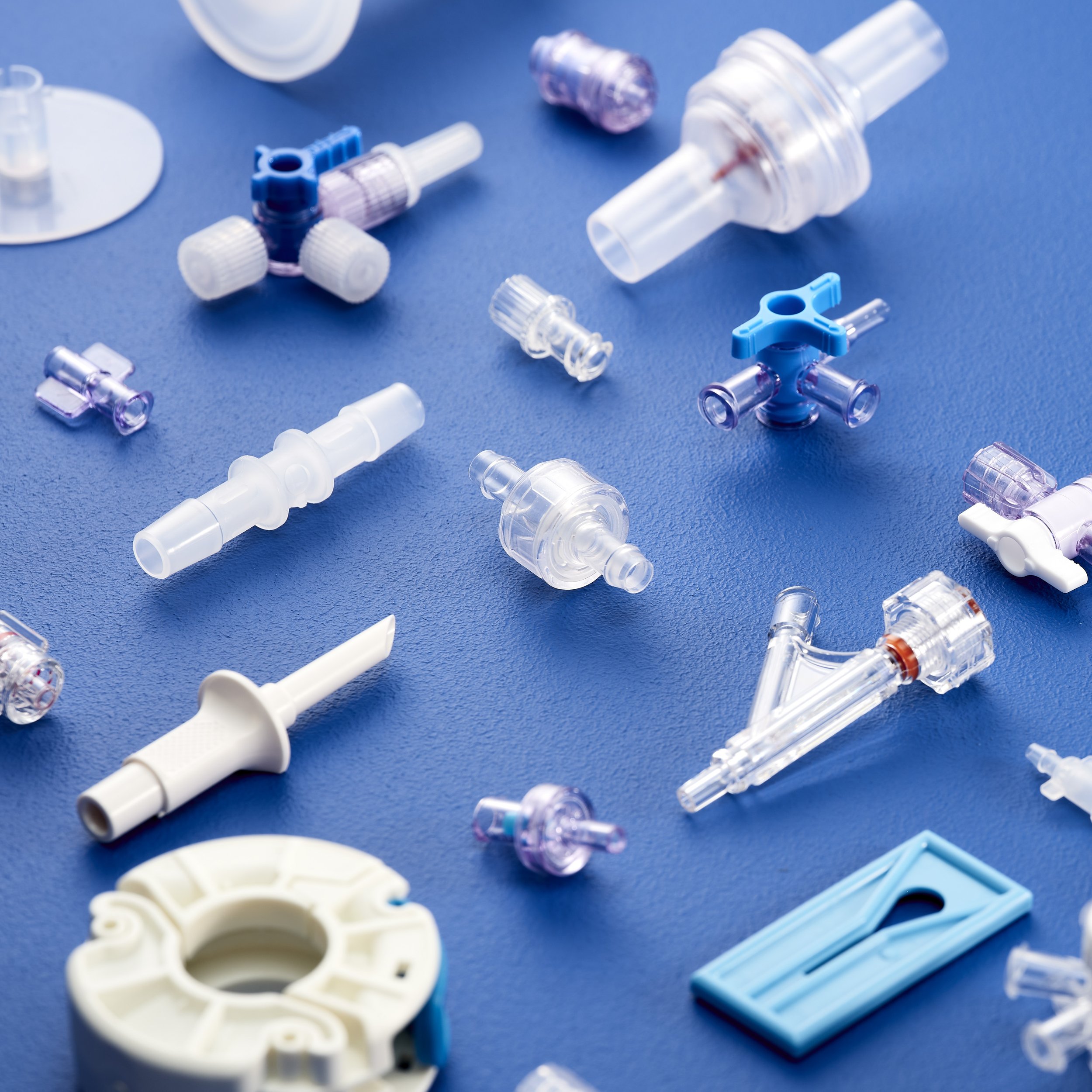 Various medical respiratory device parts, including connectors, valves, and adapters, scattered on a blue surface.
